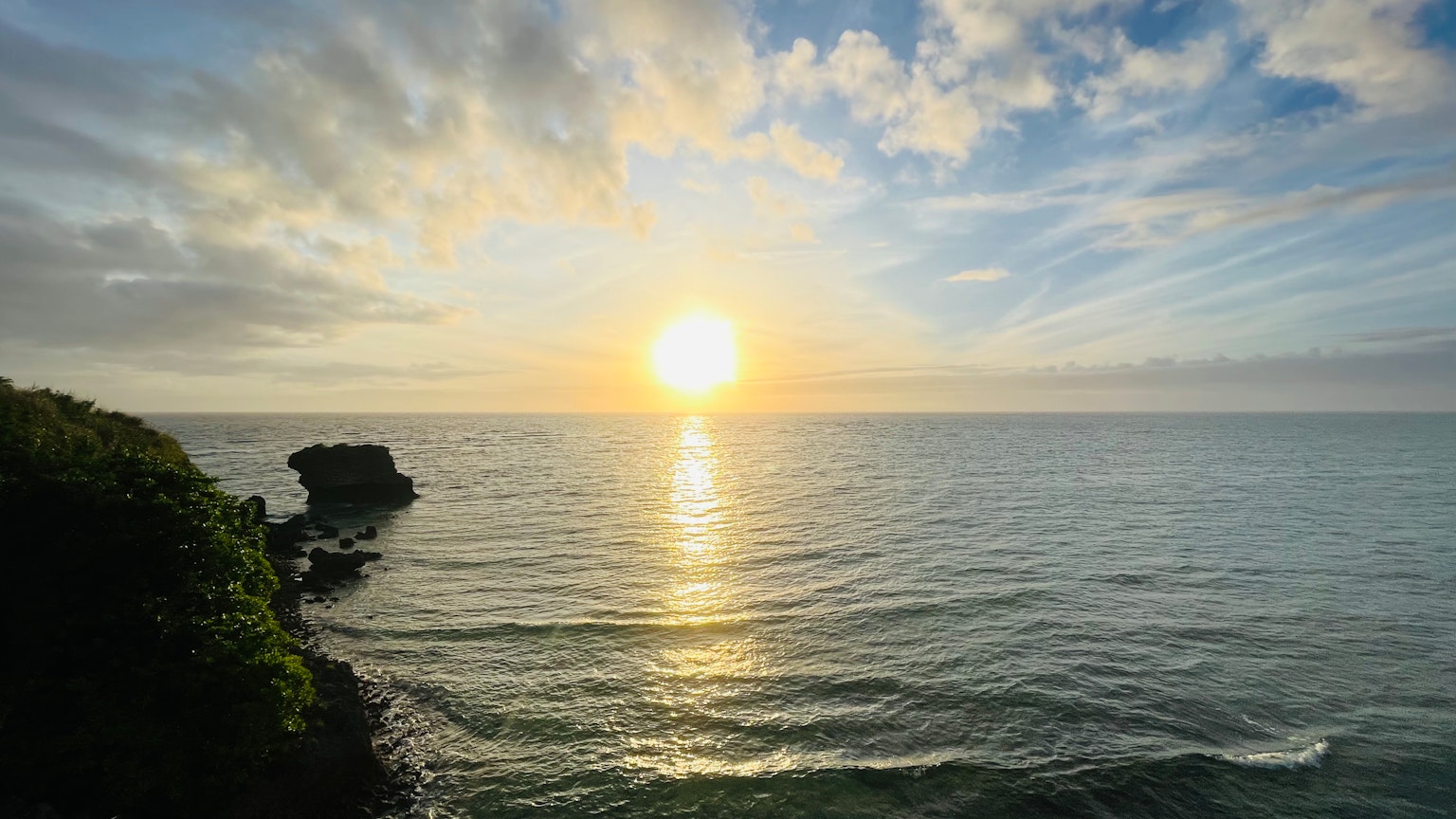 Atardecer sobre el océano con olas tranquilas y costa rocosa