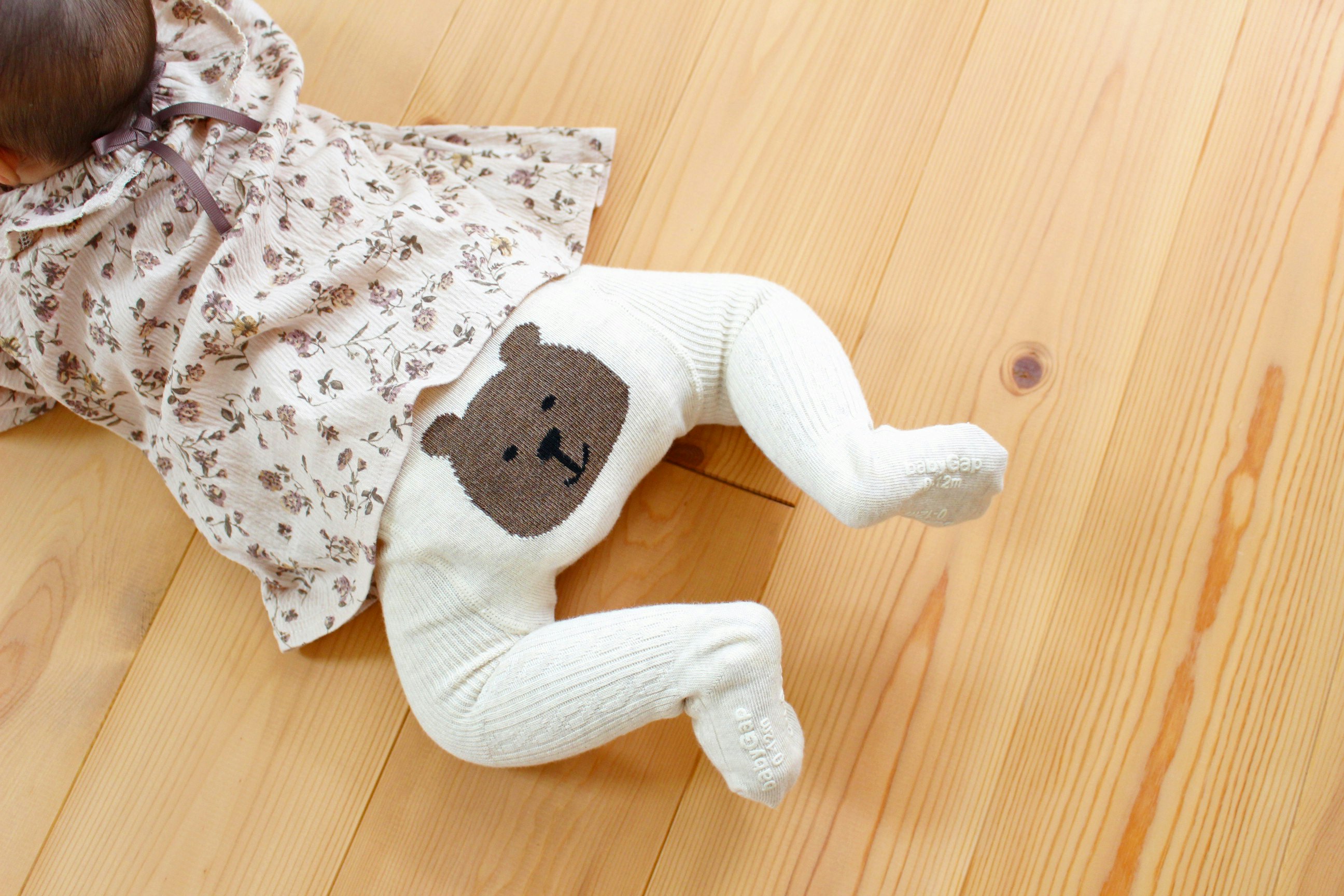 baby lying on a wooden floor with a plush toy pattern outfit