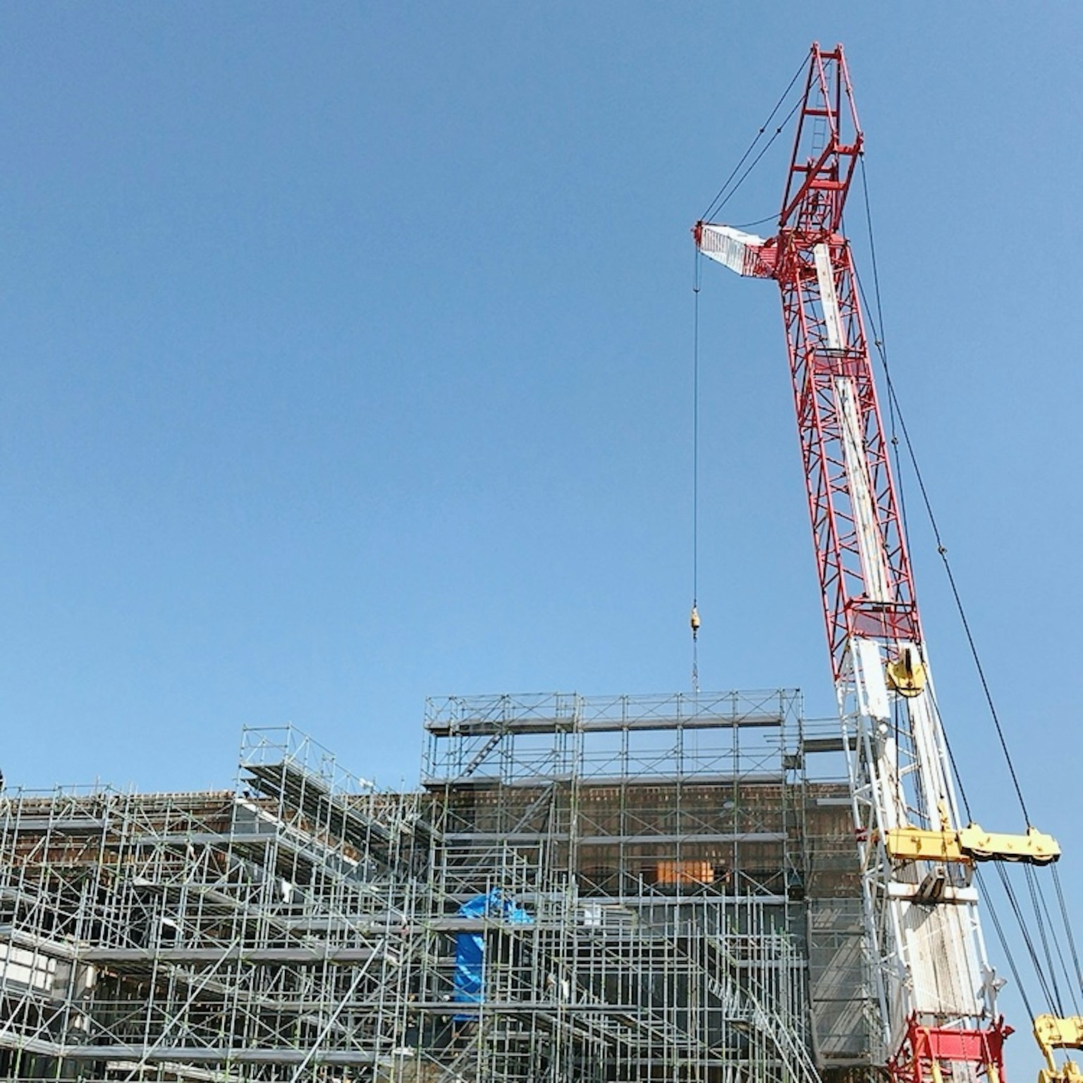 Site de construction avec échafaudage et grue sous un ciel bleu clair