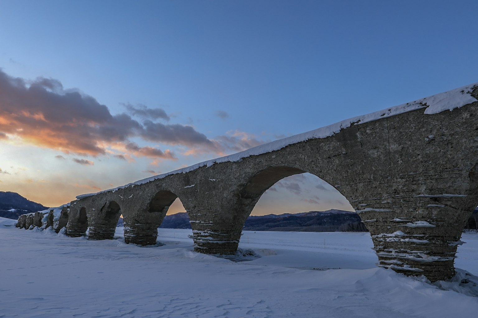 Schneebedeckter Steinbogenbrücke unter einem Sonnenuntergangshimmel