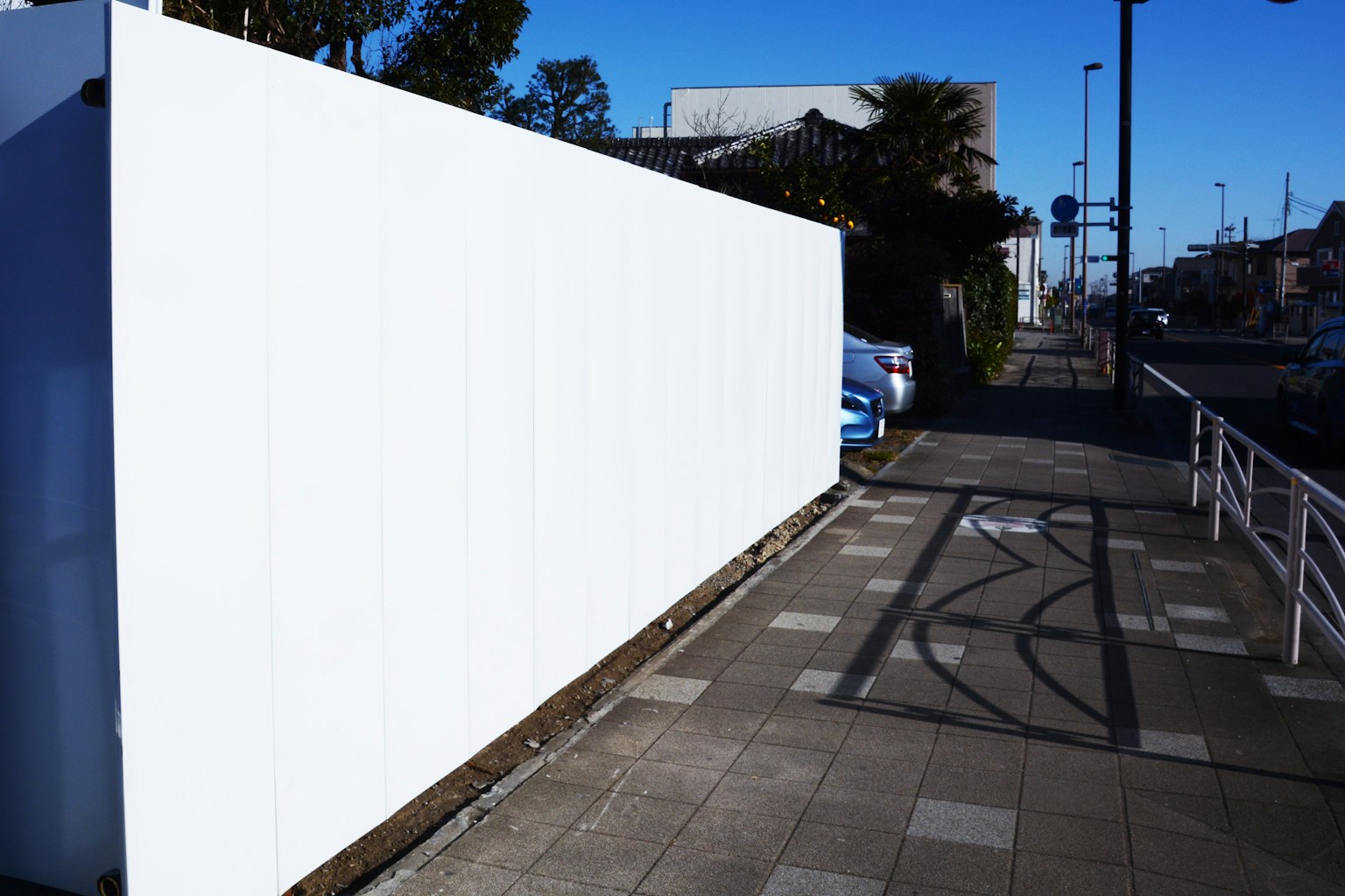 A view of a white wall alongside a paved sidewalk