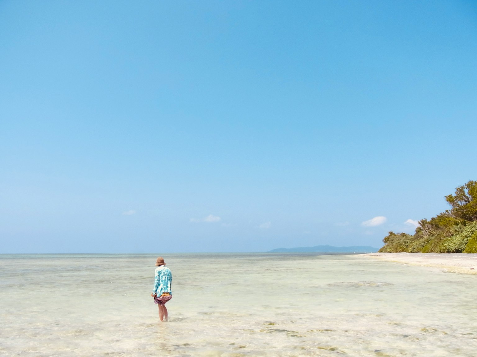 A woman standing in shallow water with a clear blue sky and distant shoreline
