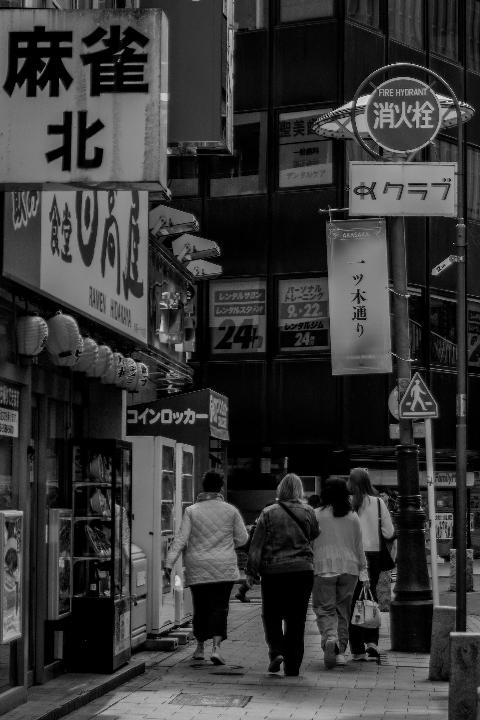 ภาพถนนขาวดำที่มีผู้คนเดินอยู่ ซอยแคบที่มีร้านค้าและป้าย
