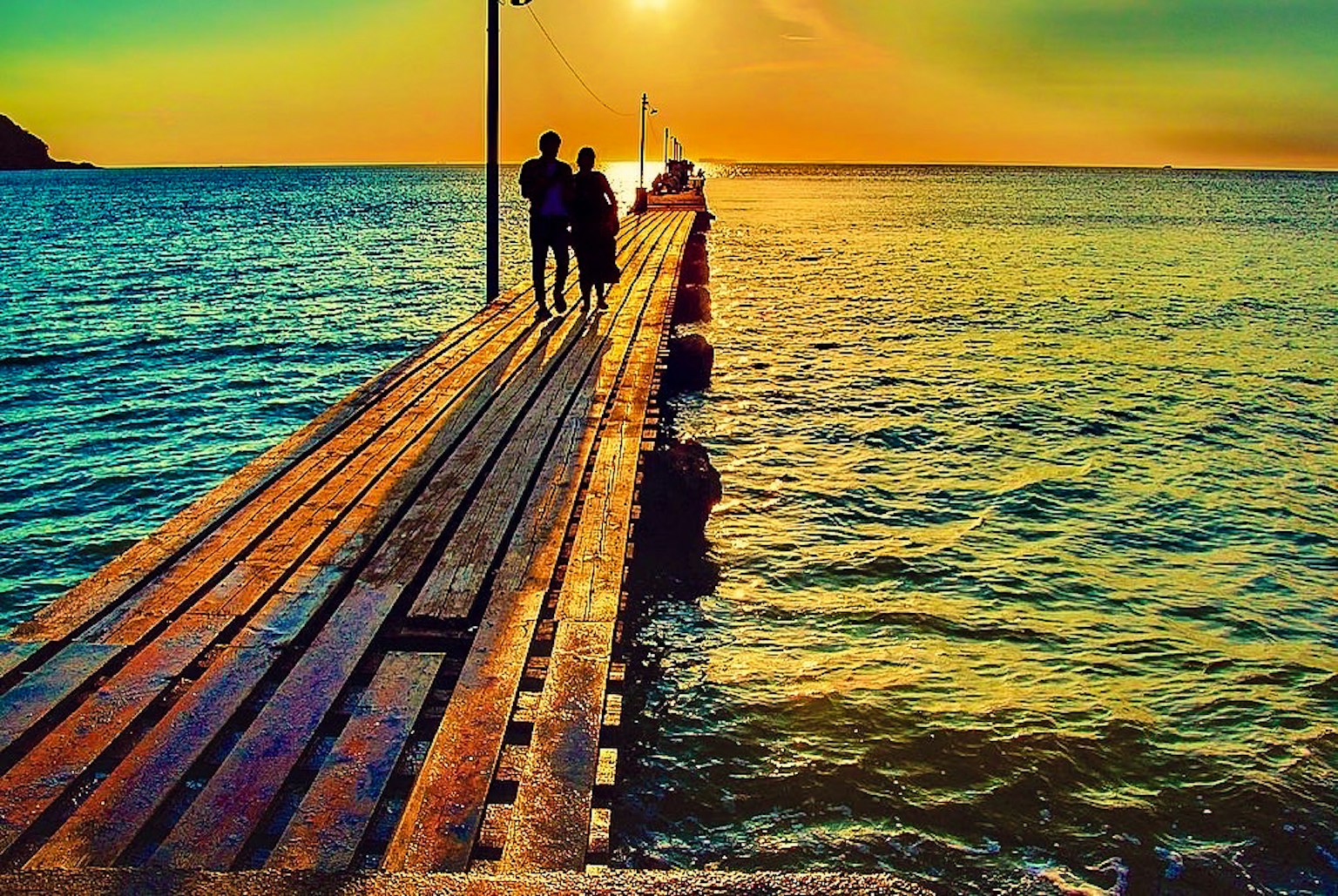 Silueta de una pareja caminando por un muelle de madera al atardecer