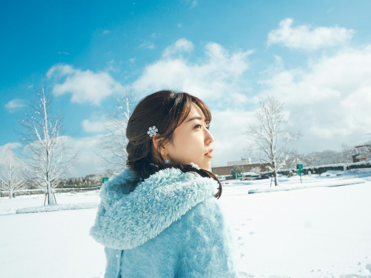 Profilo di una donna in un cappotto con cappuccio blu nella neve con cielo blu chiaro e nuvole bianche