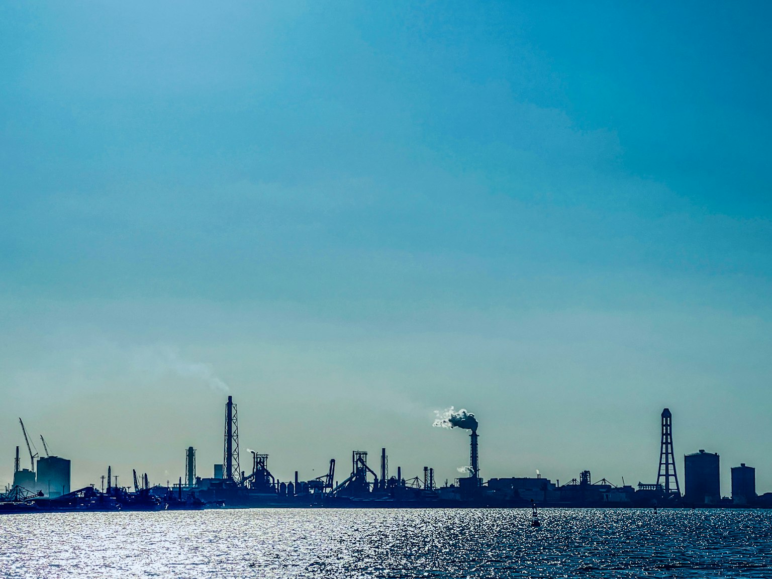 Silhouette eines Industriegebiets, das sich unter einem blauen Himmel im Wasser spiegelt