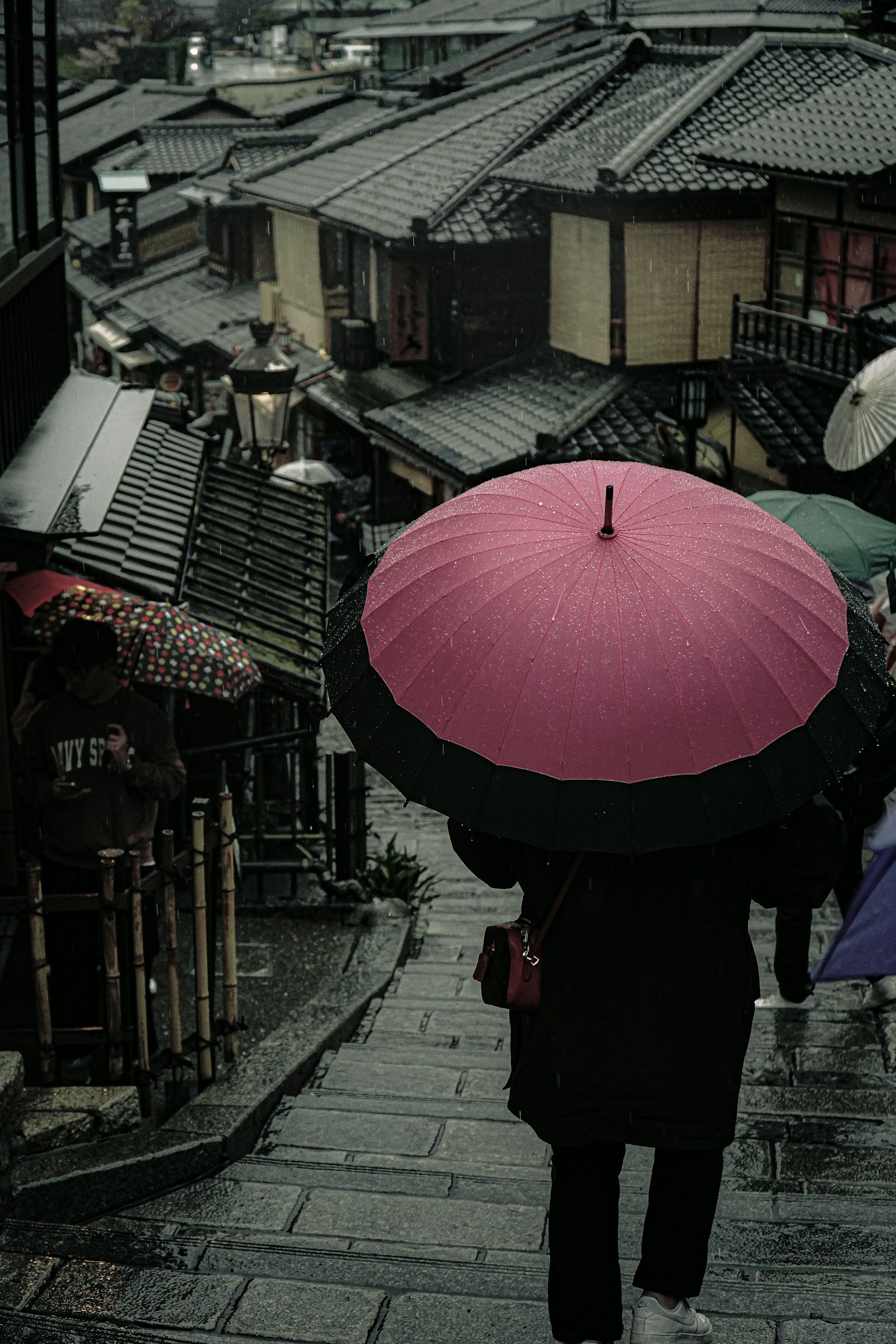 A person walking in a historic street with a large pink umbrella in the rain