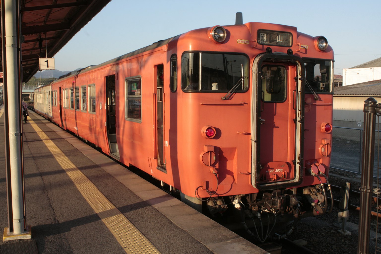 Sebuah kereta oranye yang diparkir di stasiun saat matahari terbenam