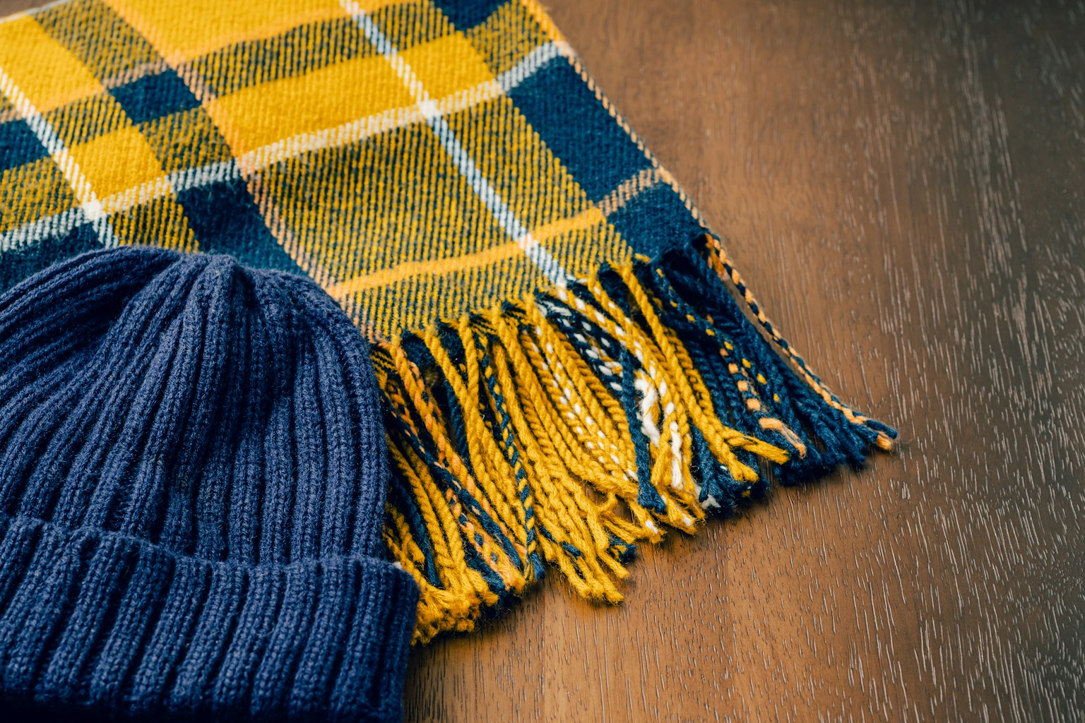 Ein gelb-blau kariertes Tuch und eine marineblaue Strickmütze liegen auf einem Holztisch