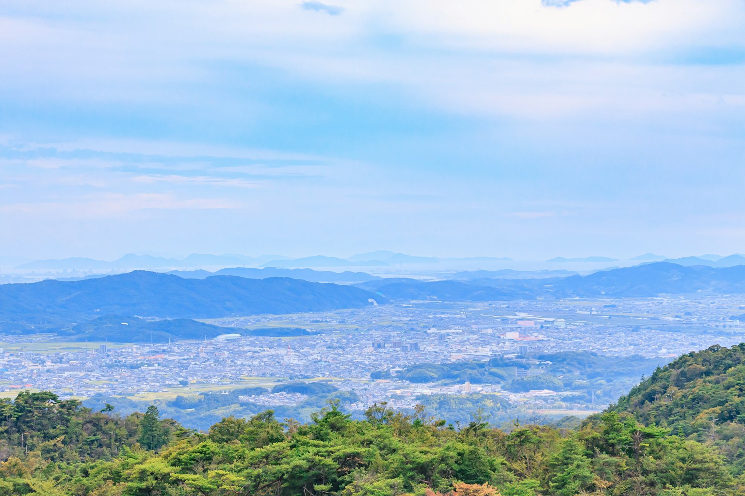 Pemandangan panorama kota dengan langit biru dan gunung hijau di latar belakang