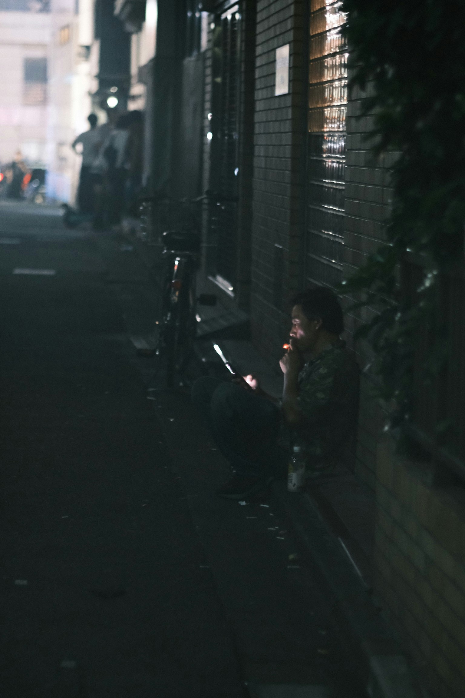 Eine Person sitzt in einer dunklen Gasse und benutzt ein Smartphone und raucht