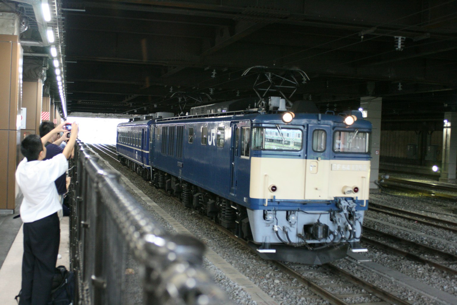 Locomotive électrique bleue dans une station souterraine avec des personnes prenant des photos
