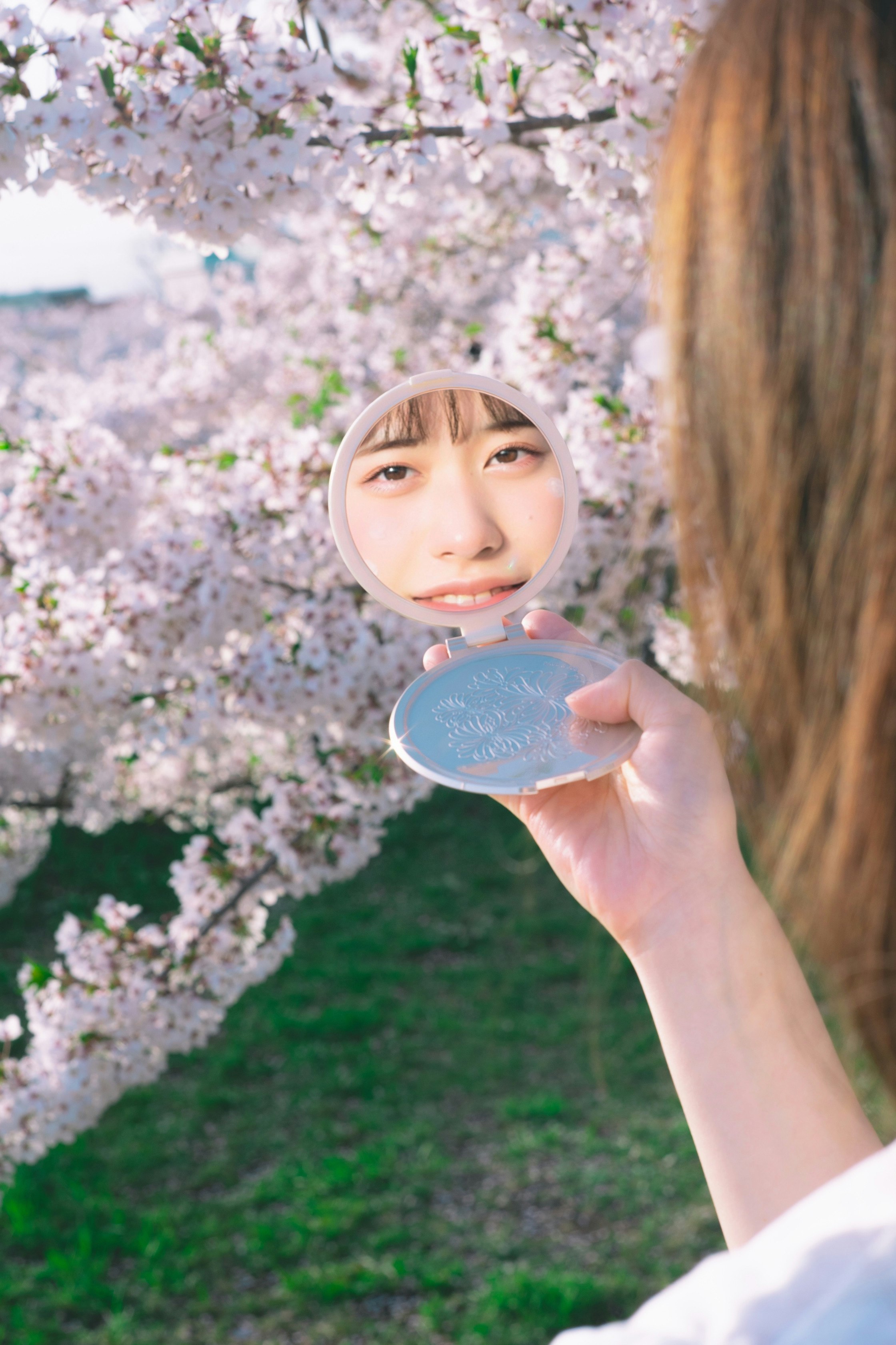 桜の花の前で鏡を持つ女性