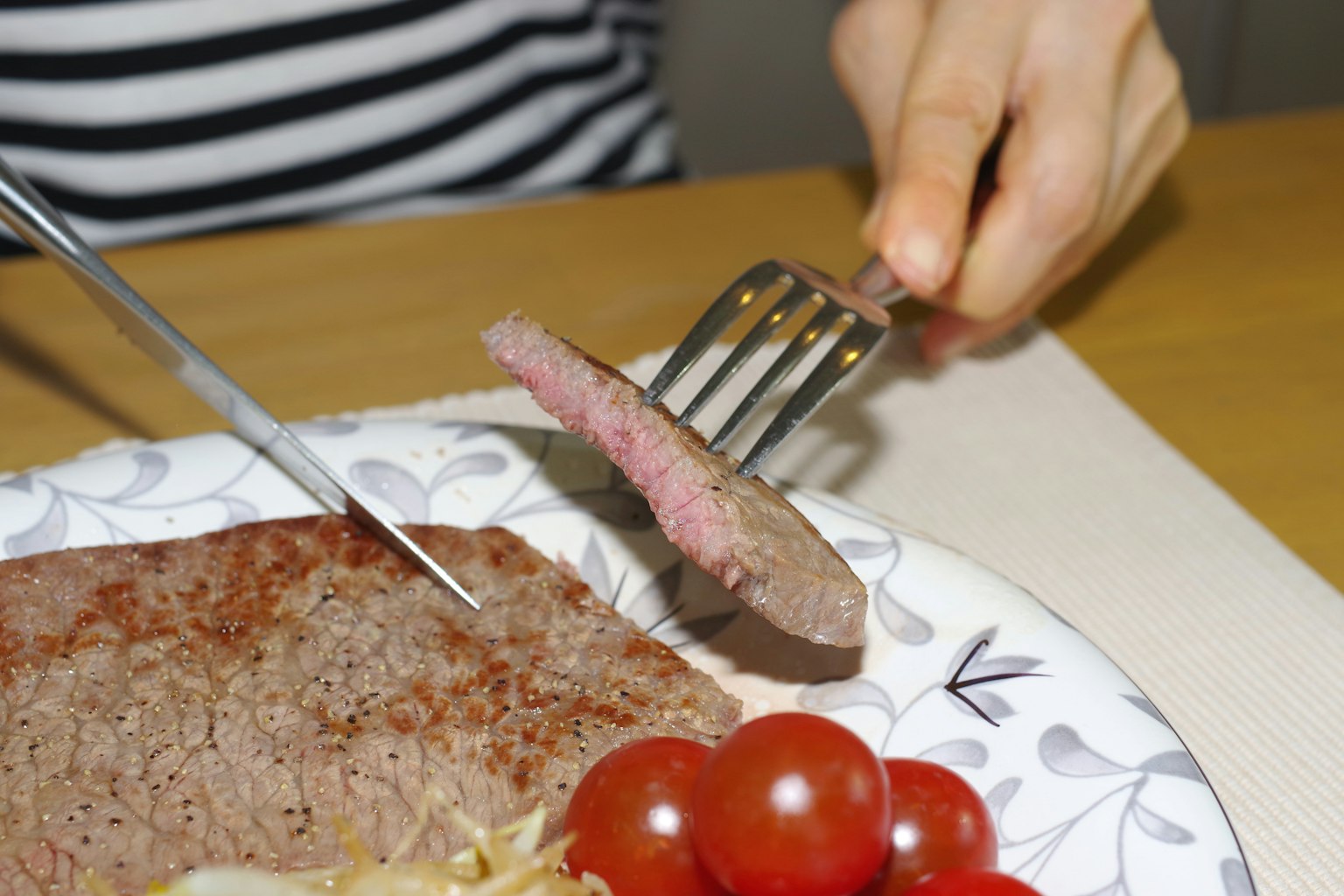 Une main coupant un morceau de viande avec une fourchette sur une assiette