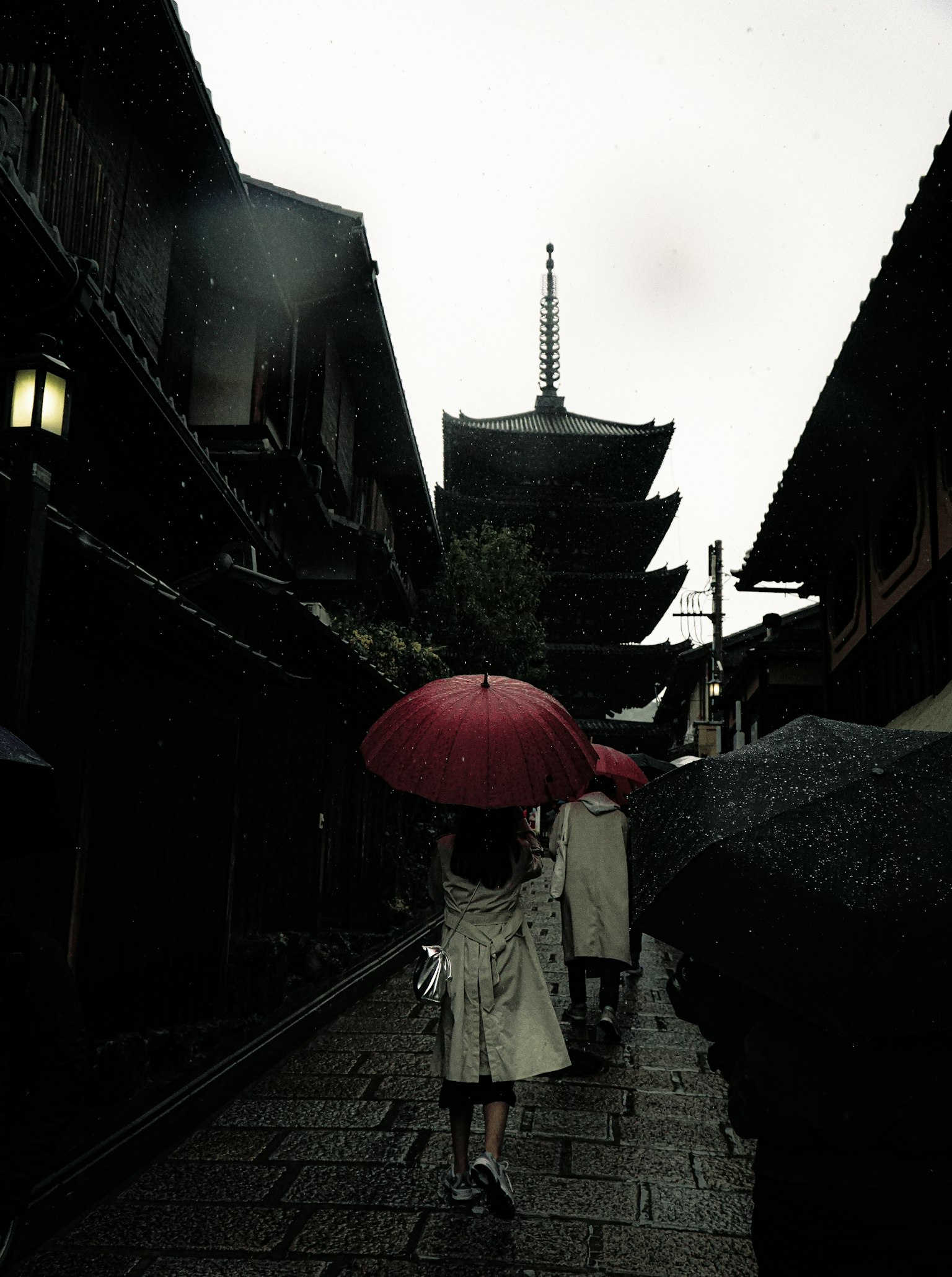 Woman with a red umbrella walking in the rain among traditional buildings
