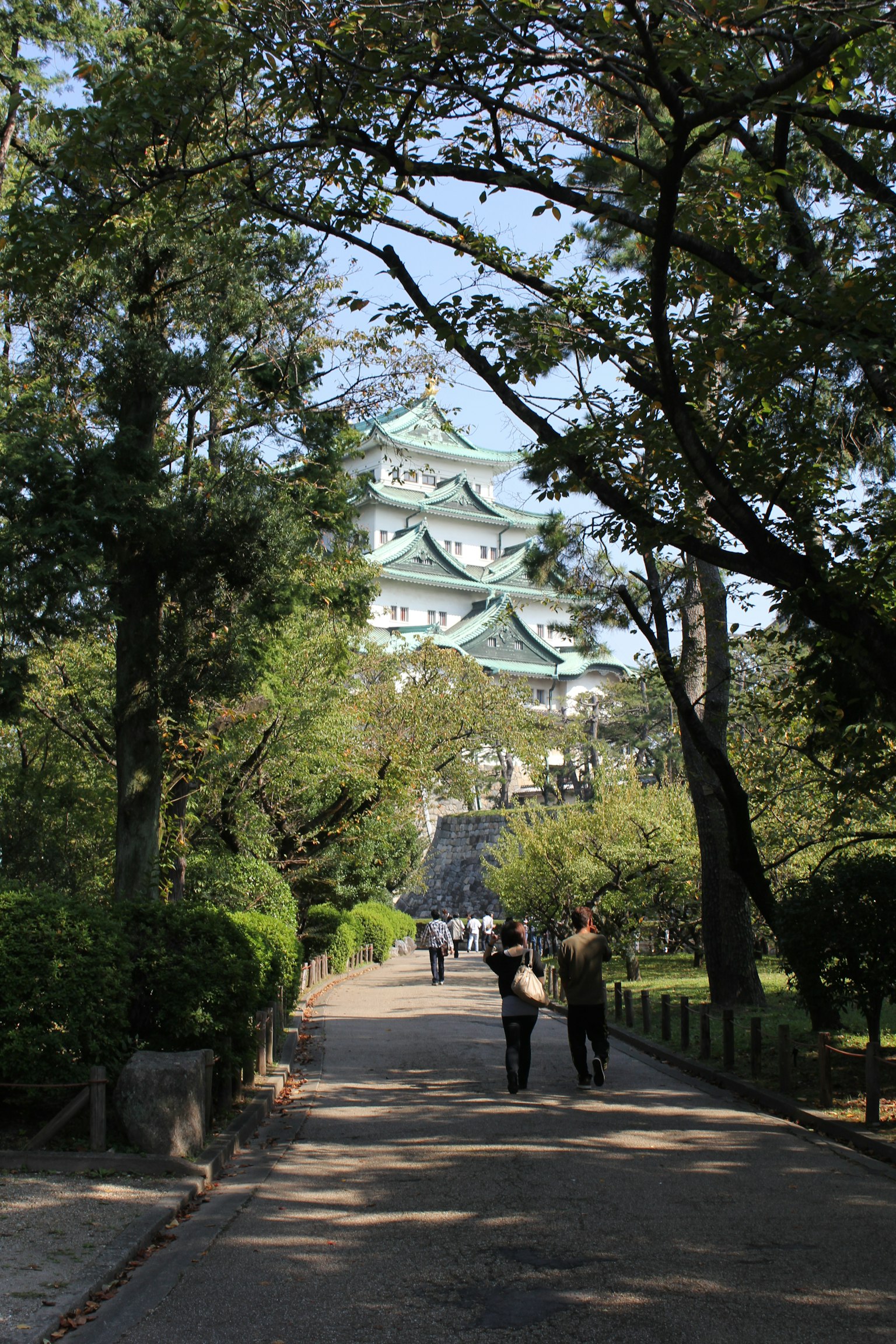 Paar, das einen von Bäumen gesäumten Weg mit dem Nagoya-Schloss im Hintergrund entlanggeht