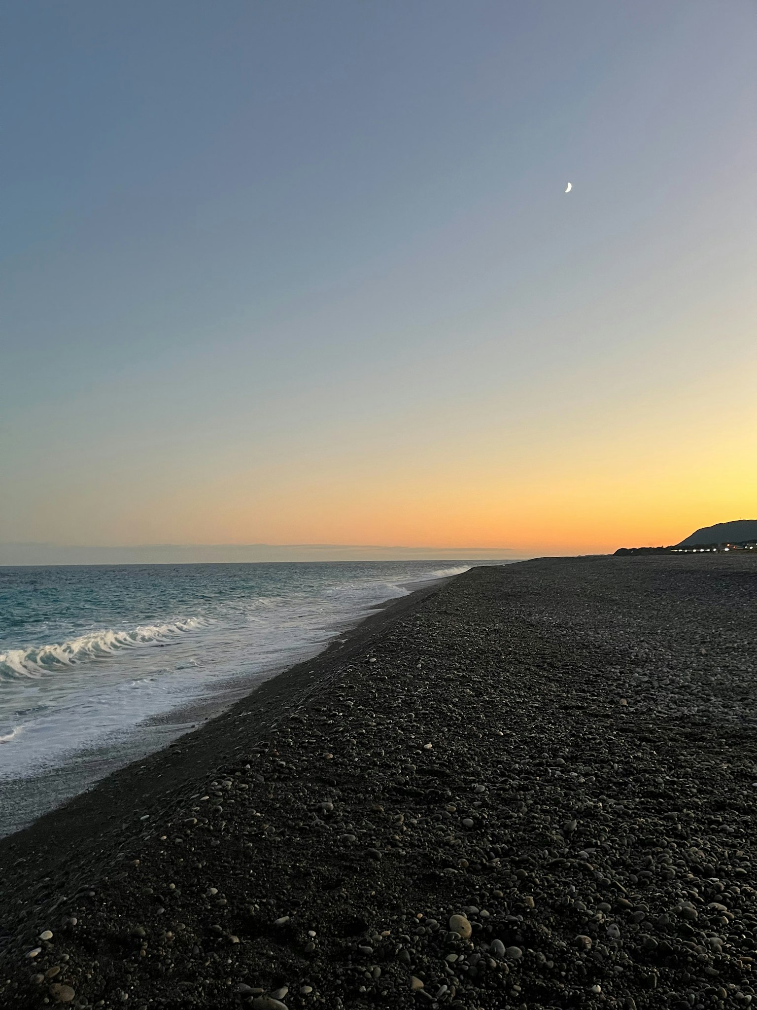 日落时的卵石海滩，轻柔的波浪和晴朗的天空