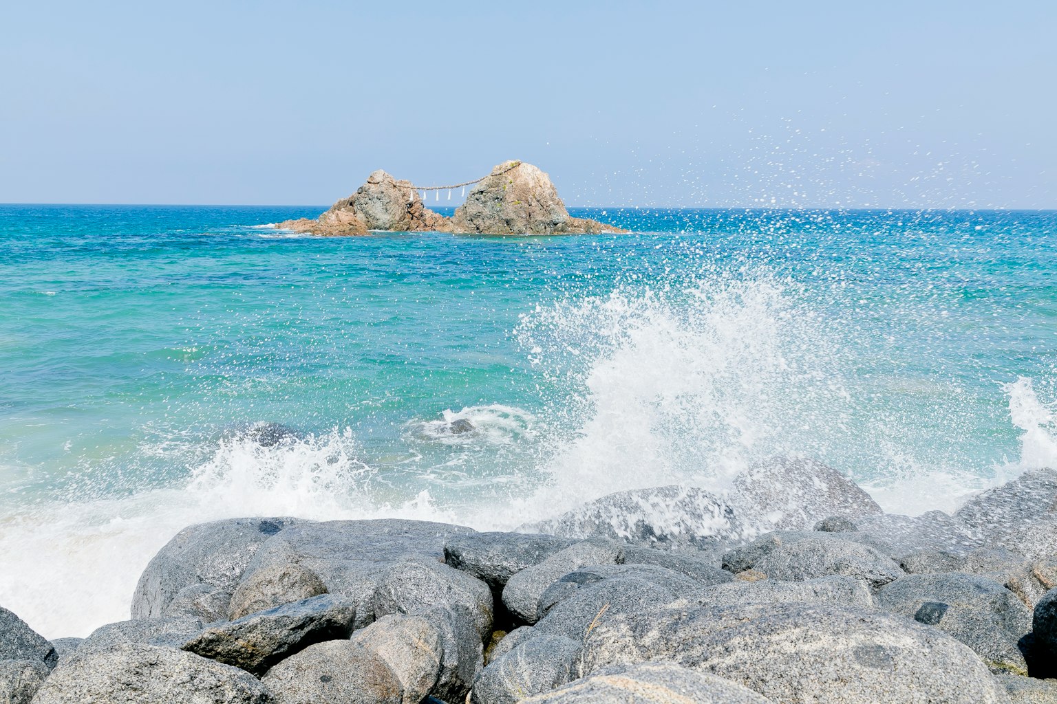 Côte rocheuse avec des vagues déferlantes et des îles lointaines dans une mer bleue claire
