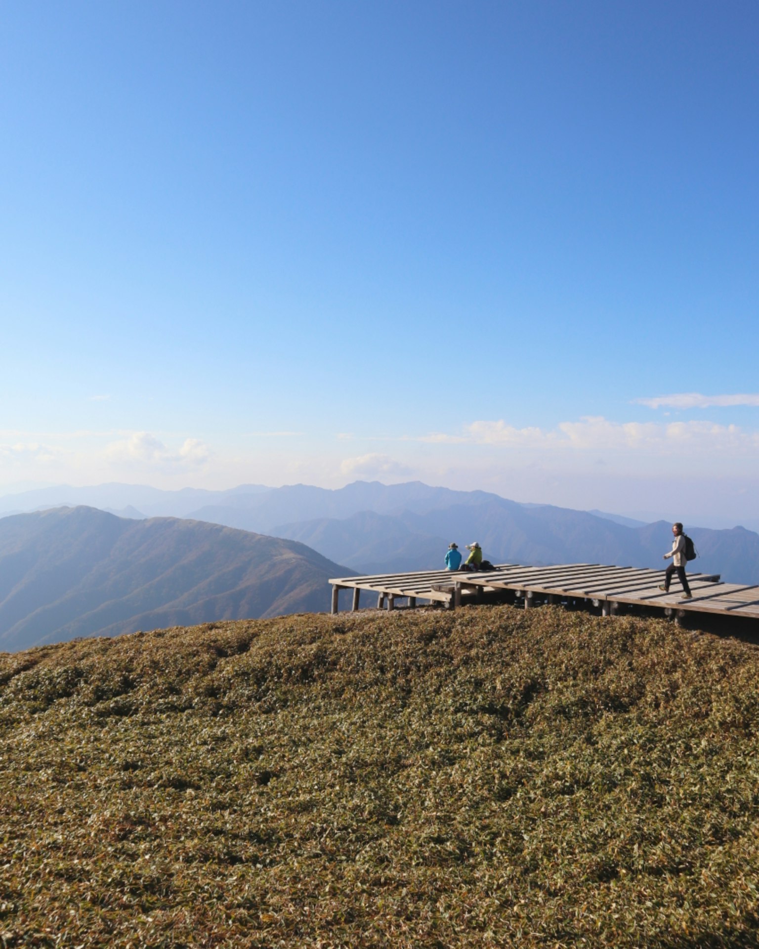 People on a mountain peak with a wooden platform under a clear blue sky