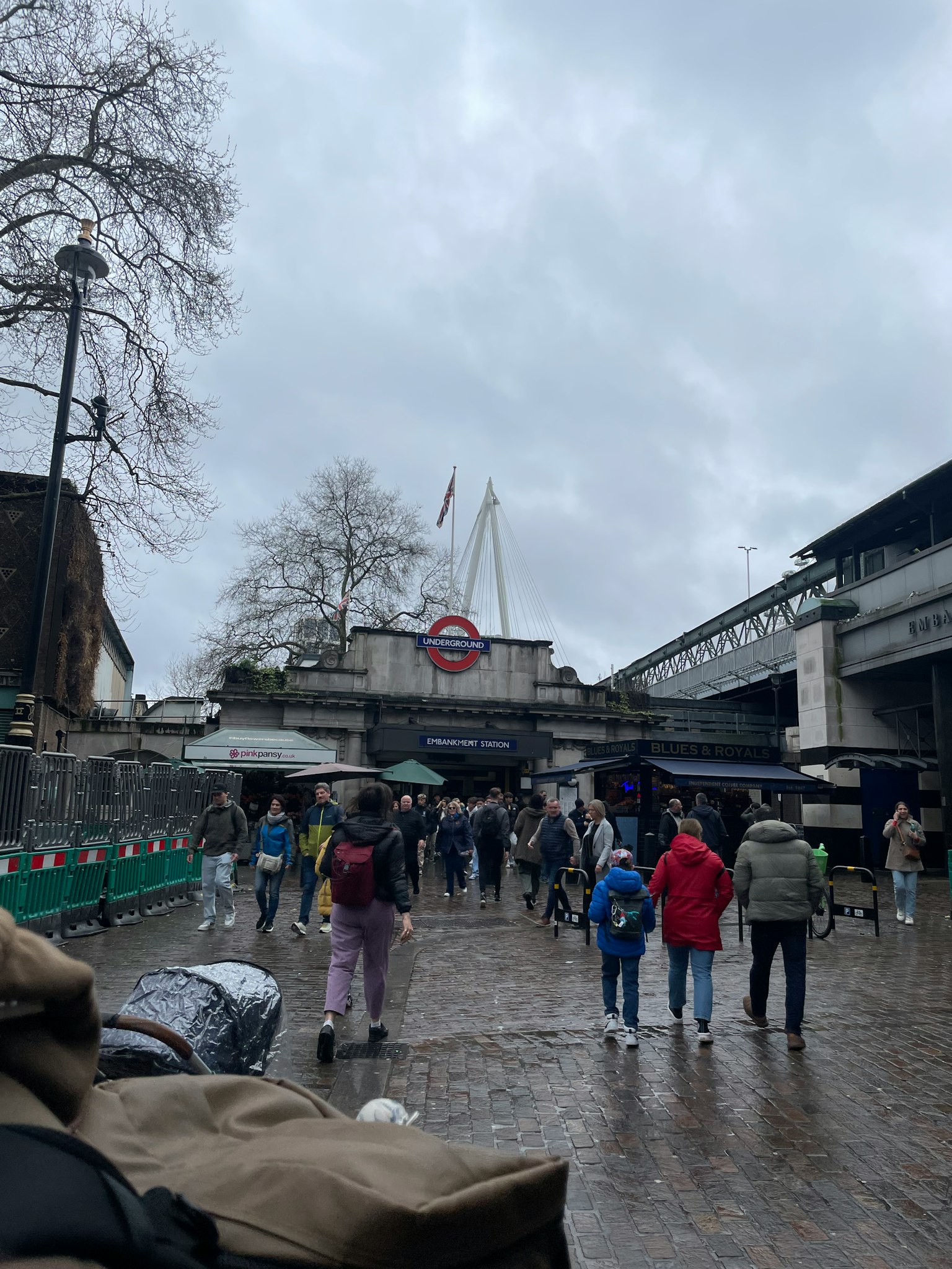 Multitud de personas frente a una estación de metro de Londres cielo nublado y suelo mojado