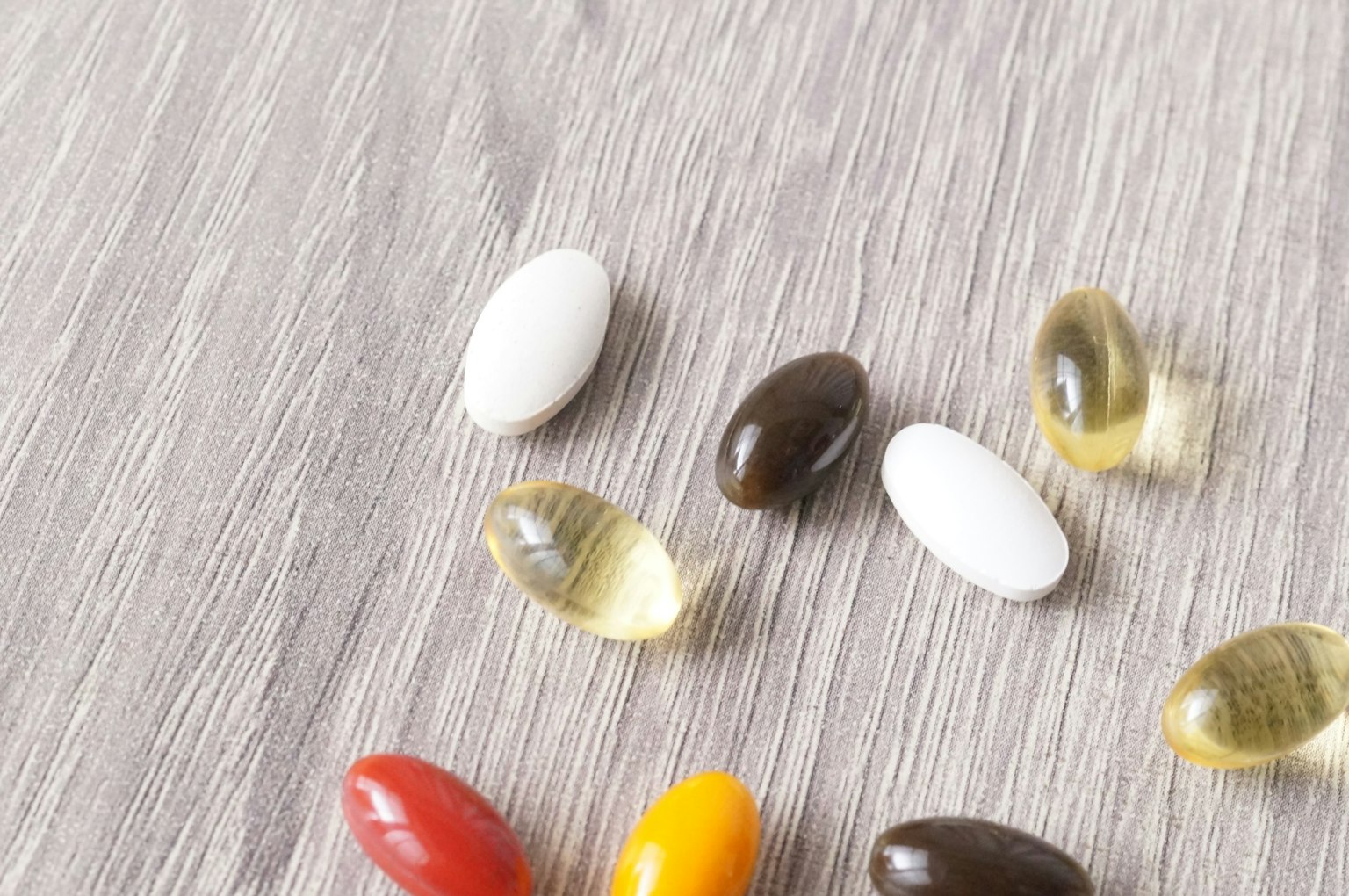 Capsule di integratori di diversi colori sparse su una superficie in legno