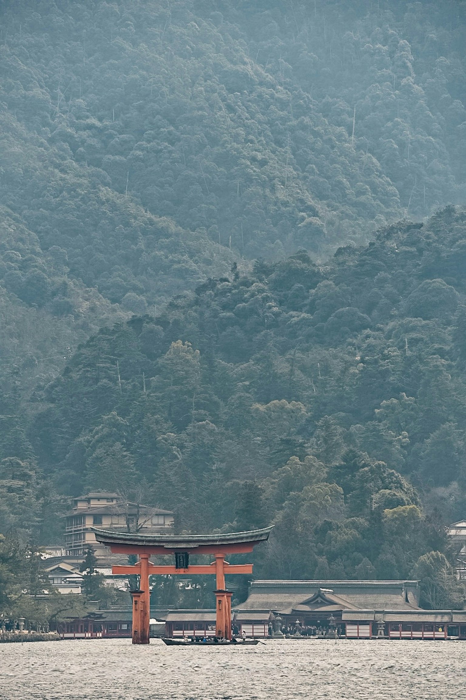 Puerta torii roja en el mar rodeada de montañas y un santuario