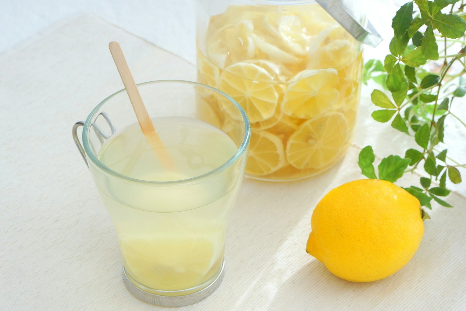 Un verre de jus de citron rafraîchissant avec un pot de tranches de citron et un citron entier sur un comptoir de cuisine propre