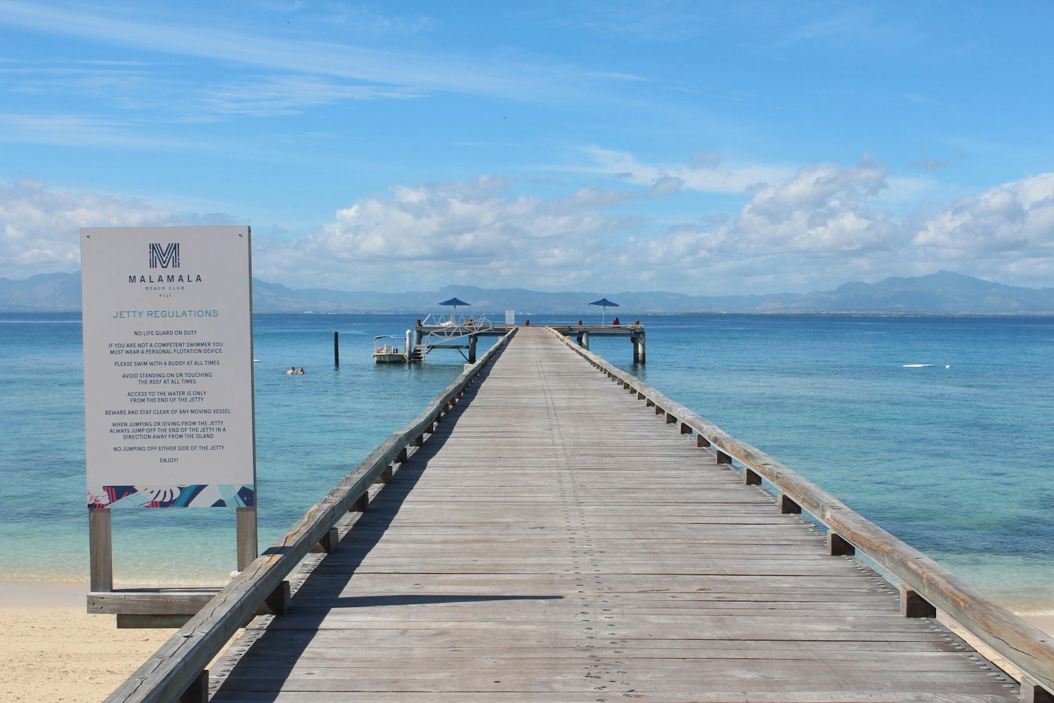 Holzsteg, der sich unter klarem Himmel ins blaue Meer erstreckt