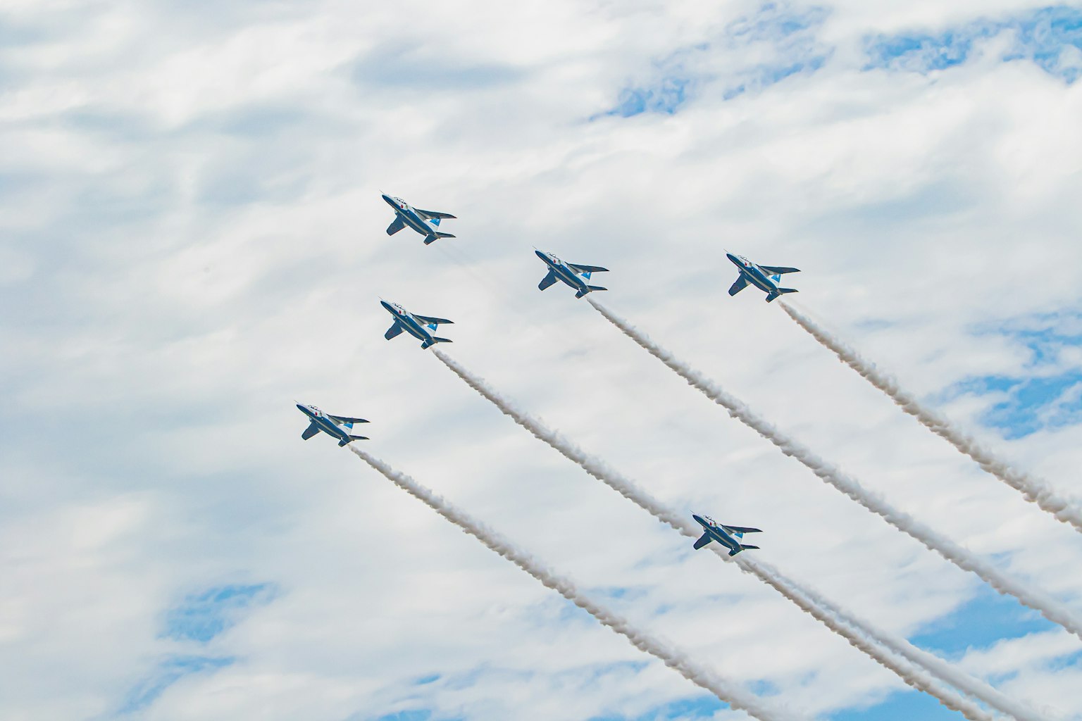Pesawat militer biru terbang dalam formasi di latar belakang langit berawan