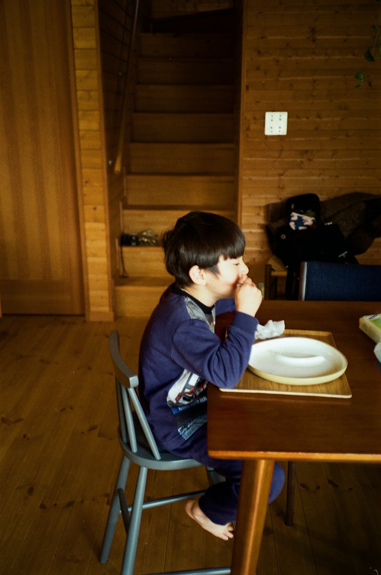 Side profile of a child enjoying a meal at a wooden table