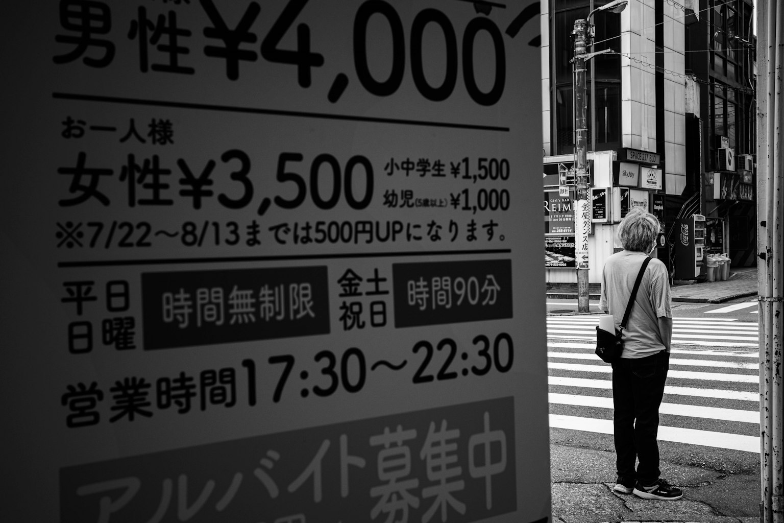 Une femme debout à un coin de rue avec un panneau affichant des prix et des horaires