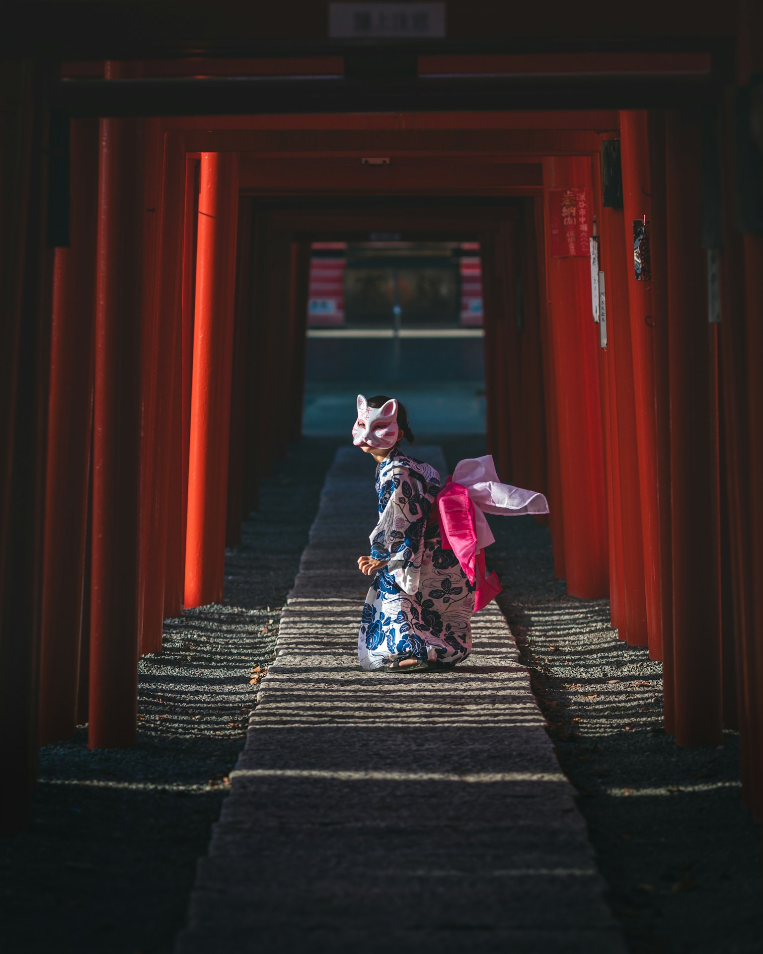 Wanita berpakaian kimono berjalan melalui gerbang torii merah dengan kuil di latar belakang