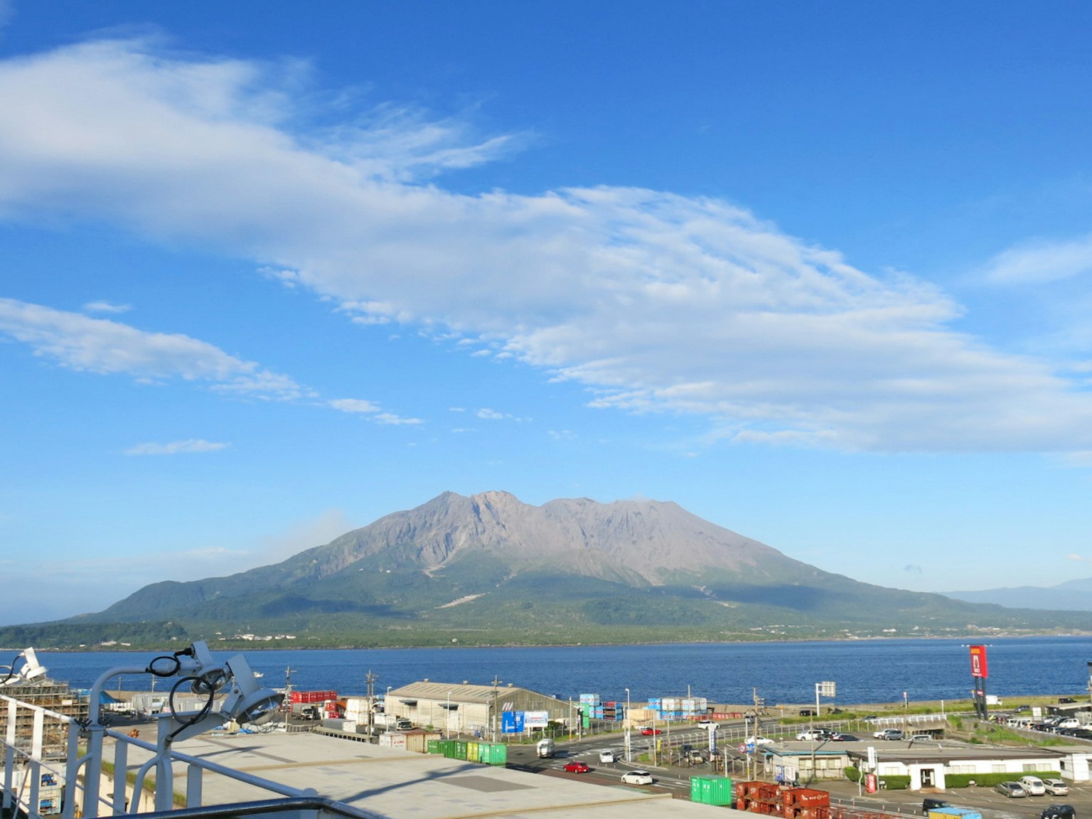 Scenic view featuring a mountain under a blue sky with clouds and a coastline