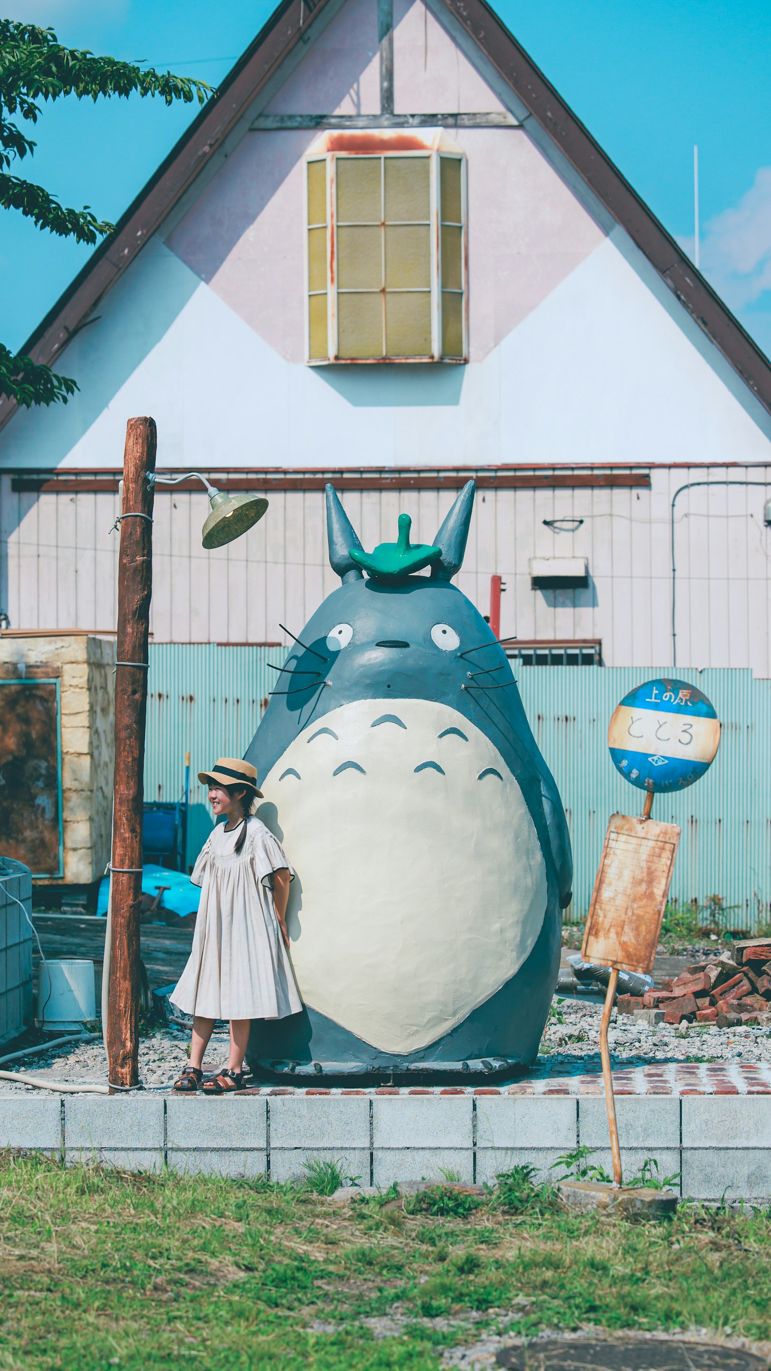 Scena con una grande statua di Totoro blu e una donna in abito bianco accanto