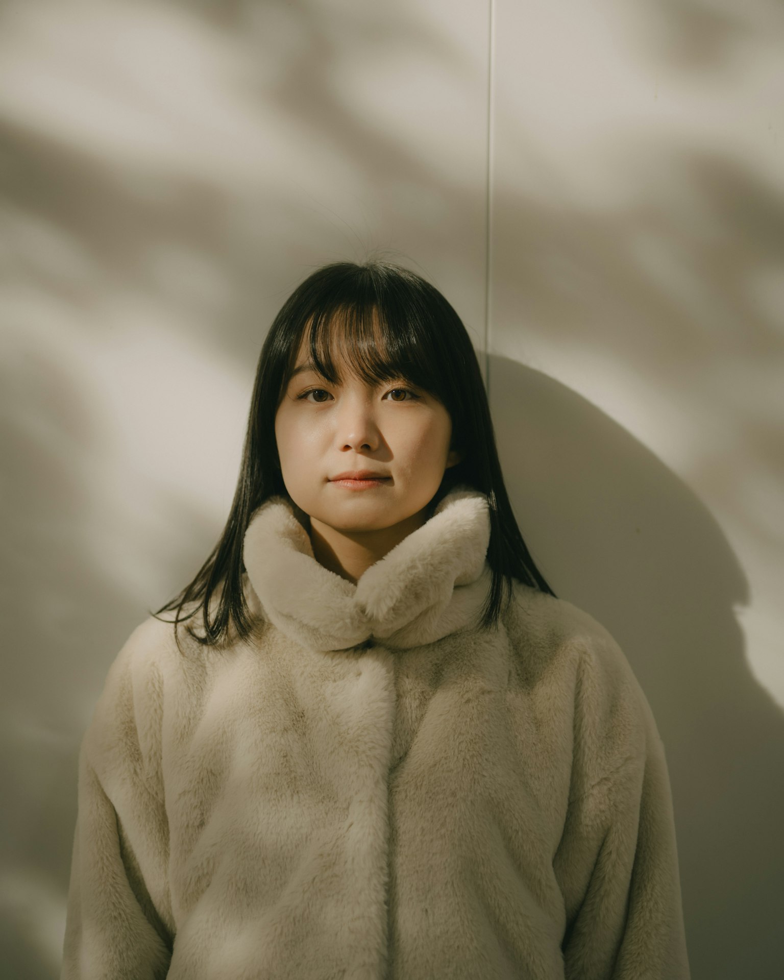부드러운 모피 코트를 입은 여성이 벽 앞에 서 있다