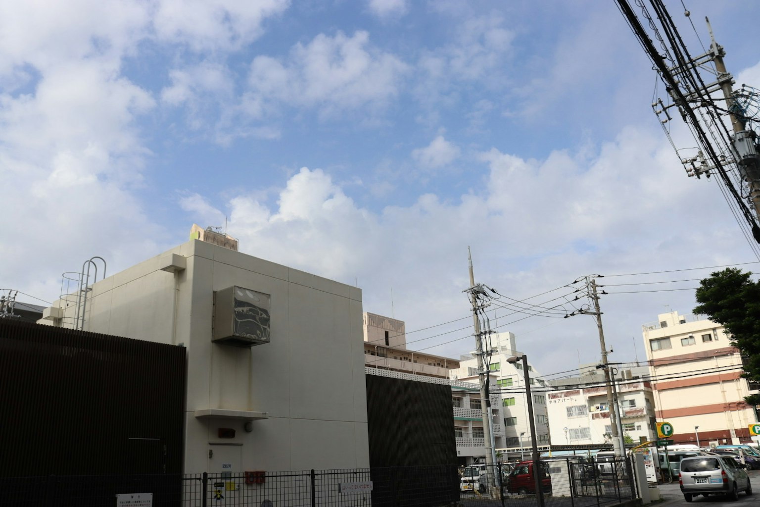 Building exterior under a blue sky with clouds and utility poles