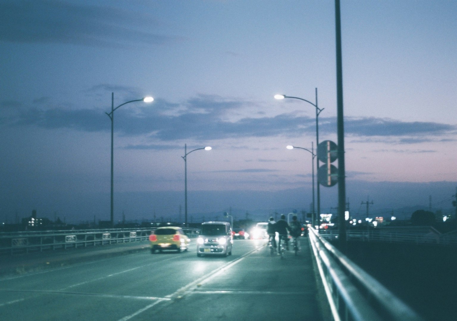 Coches circulando por un puente al anochecer con luces de calle iluminando la escena