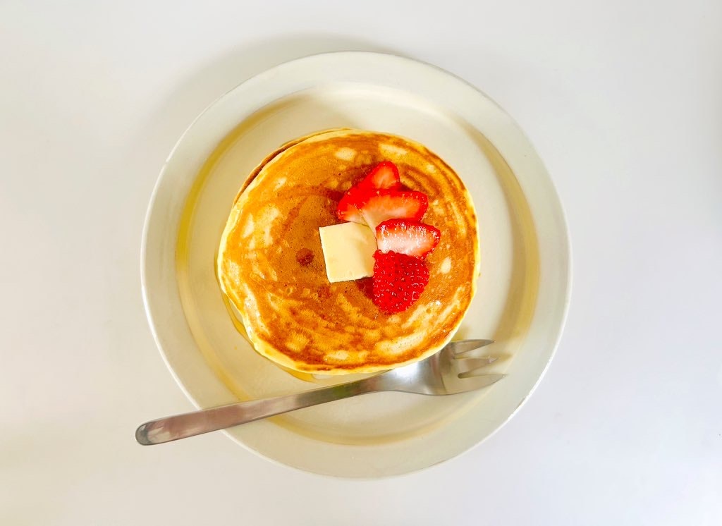 白い皿の上にパンケーキがあり、上にバターとイチゴがトッピングされている