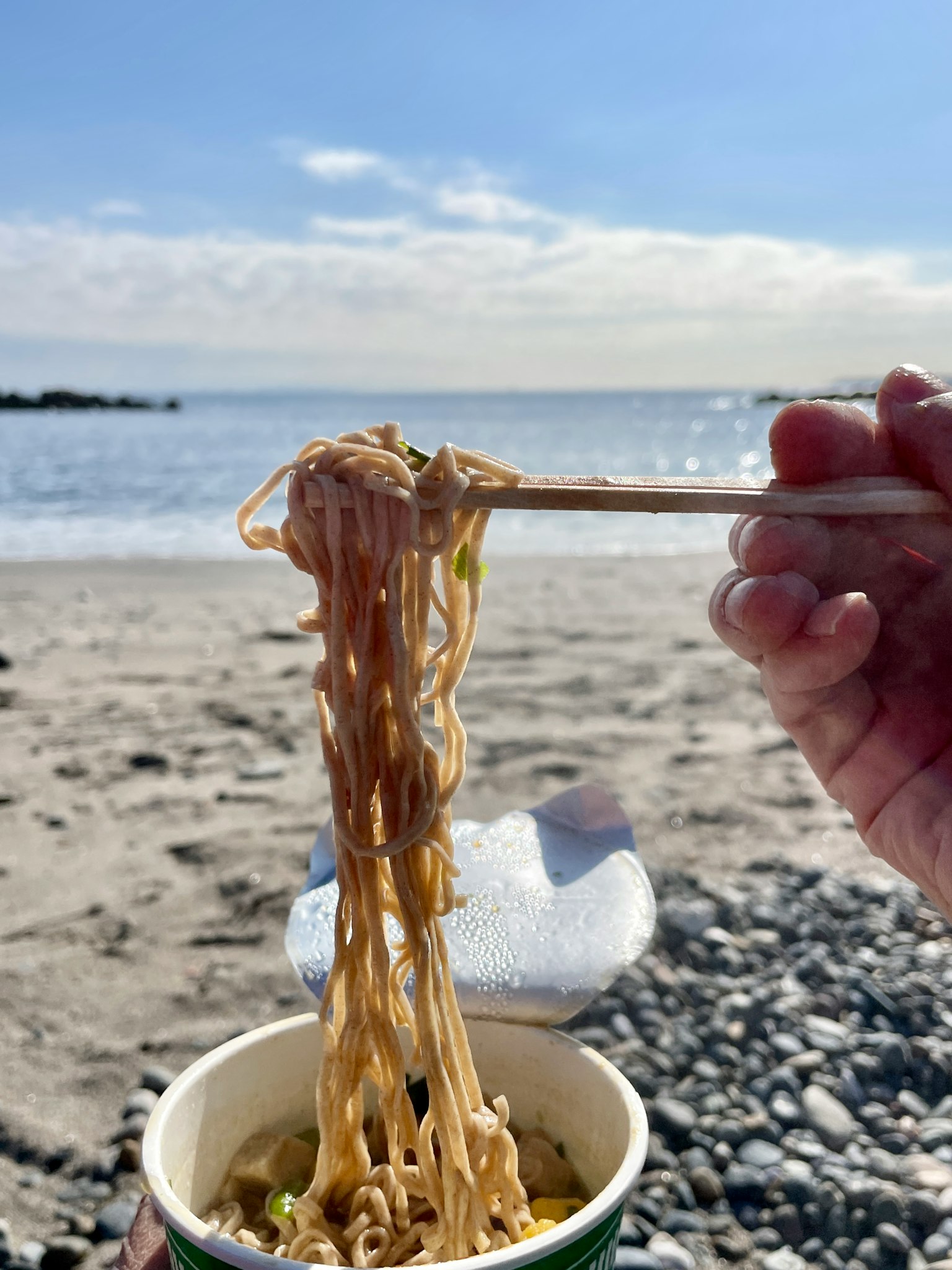 Main tenant des nouilles d'un gobelet sur la plage avec vue sur l'océan