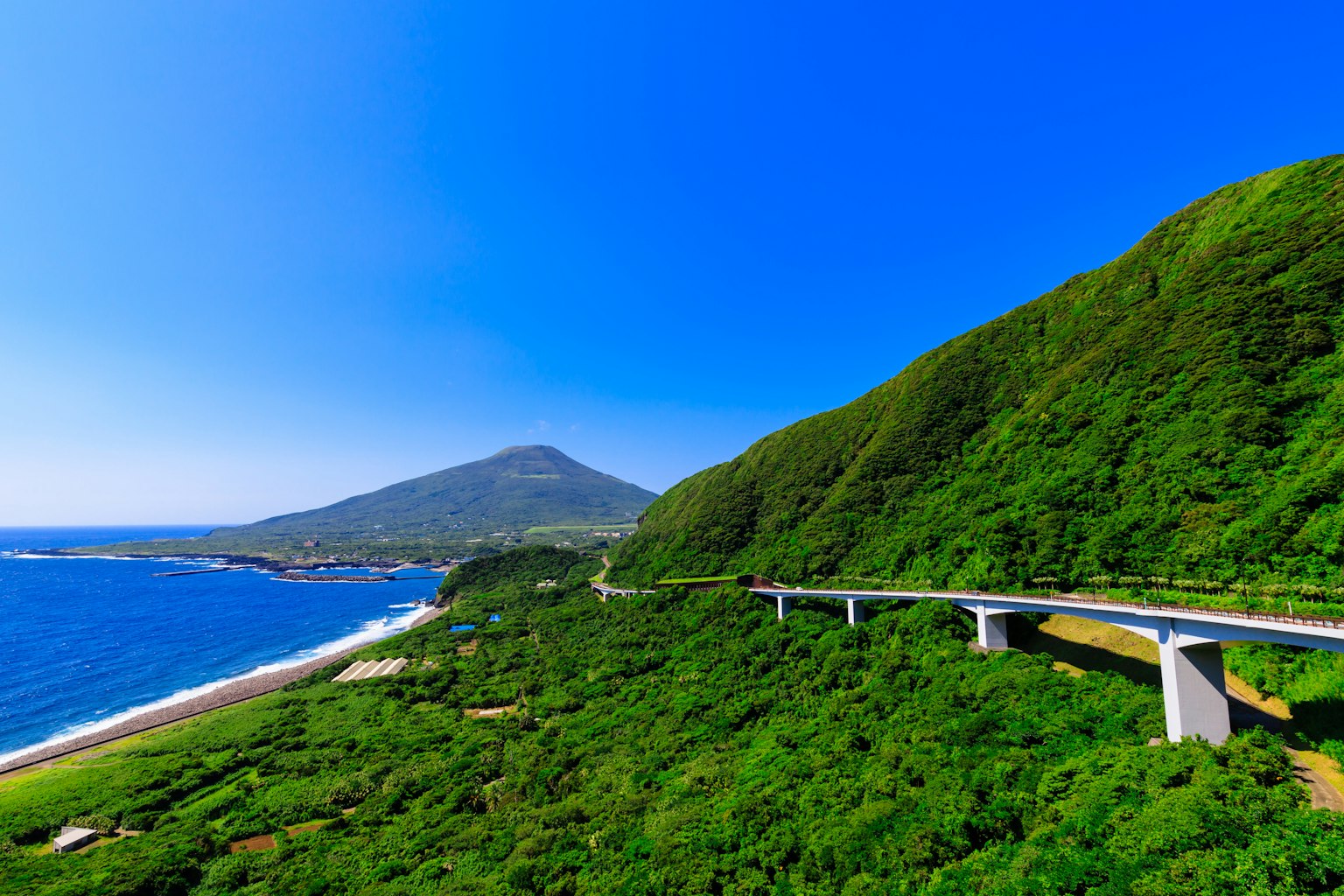 Paysage de montagnes verdoyantes et de mer bleue avec une route sur un pont à proximité