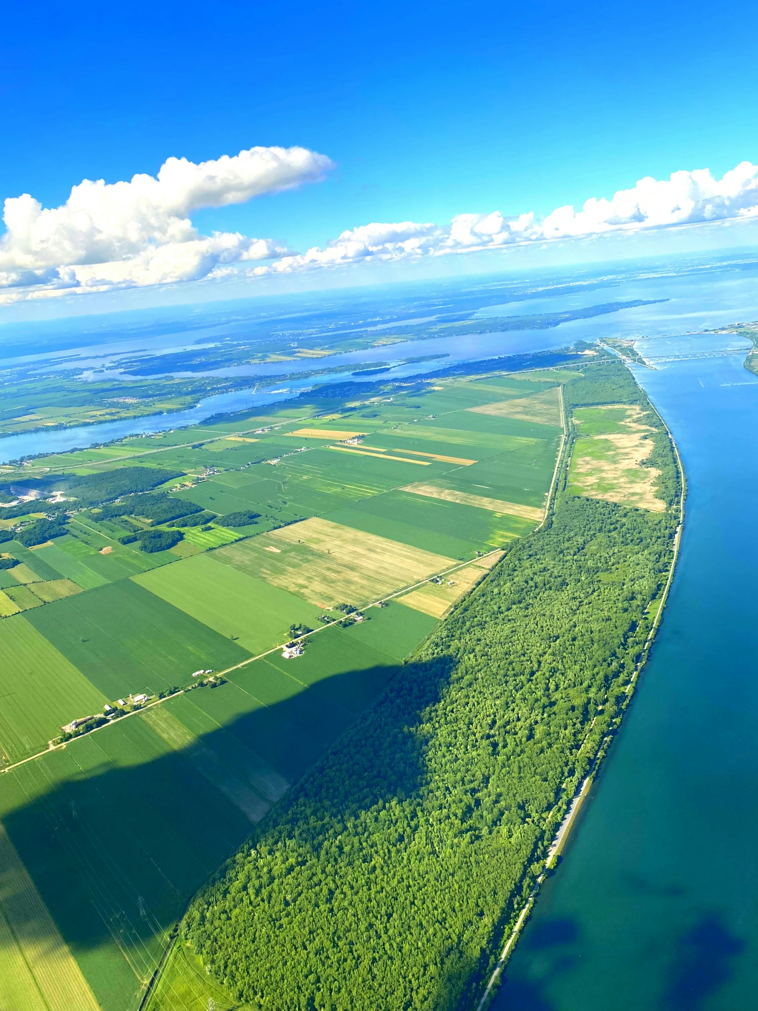 Vista ampia di terreni agricoli verdi e un fiume tortuoso sotto un cielo blu con nuvole sparse