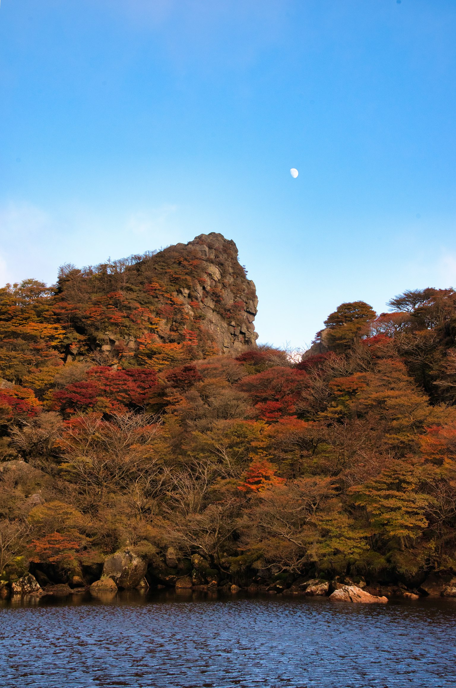青空の下に紅葉した山と月が見える風景