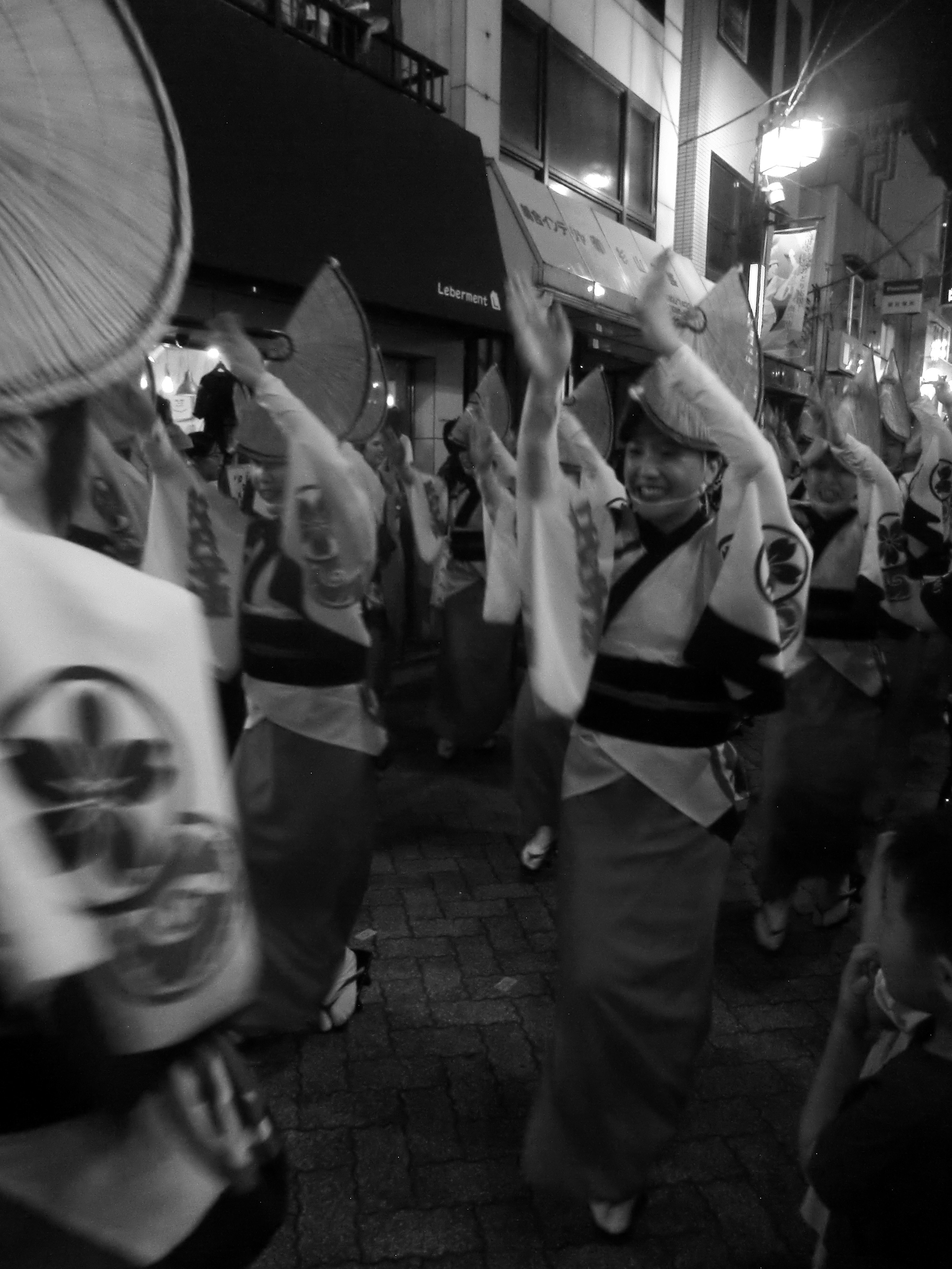 夜の商店街で阿波踊りの衣装を掲げる人々の行列