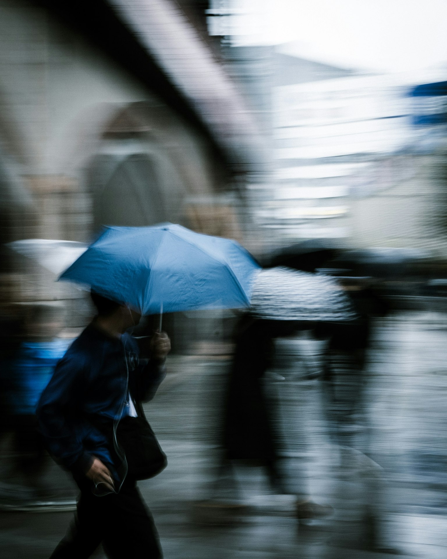 Une personne tenant un parapluie bleu se précipite sous la pluie dans une scène urbaine floue