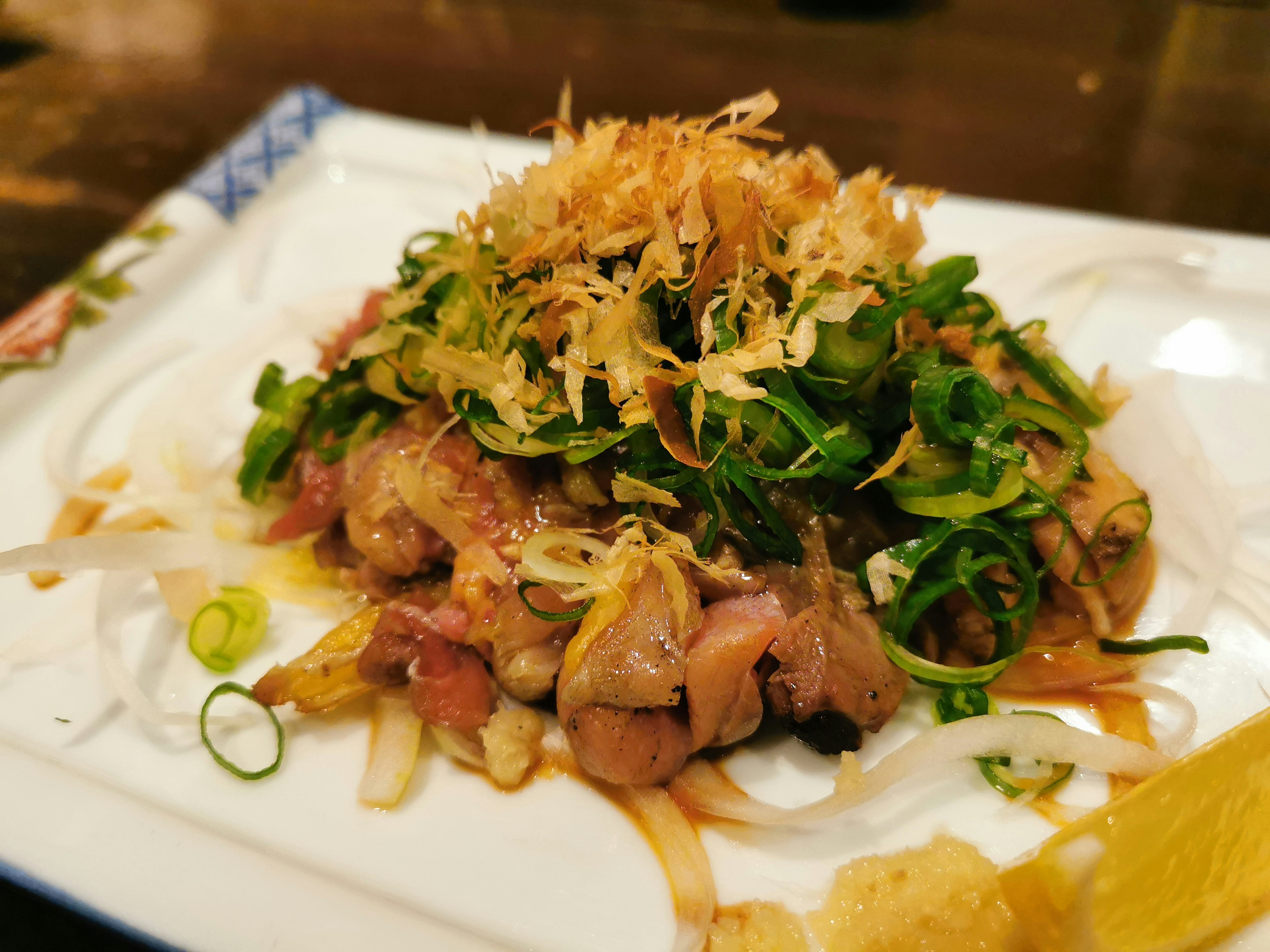 皿に盛られた肉料理と刻みネギ、揚げ玉のトッピングのある一品