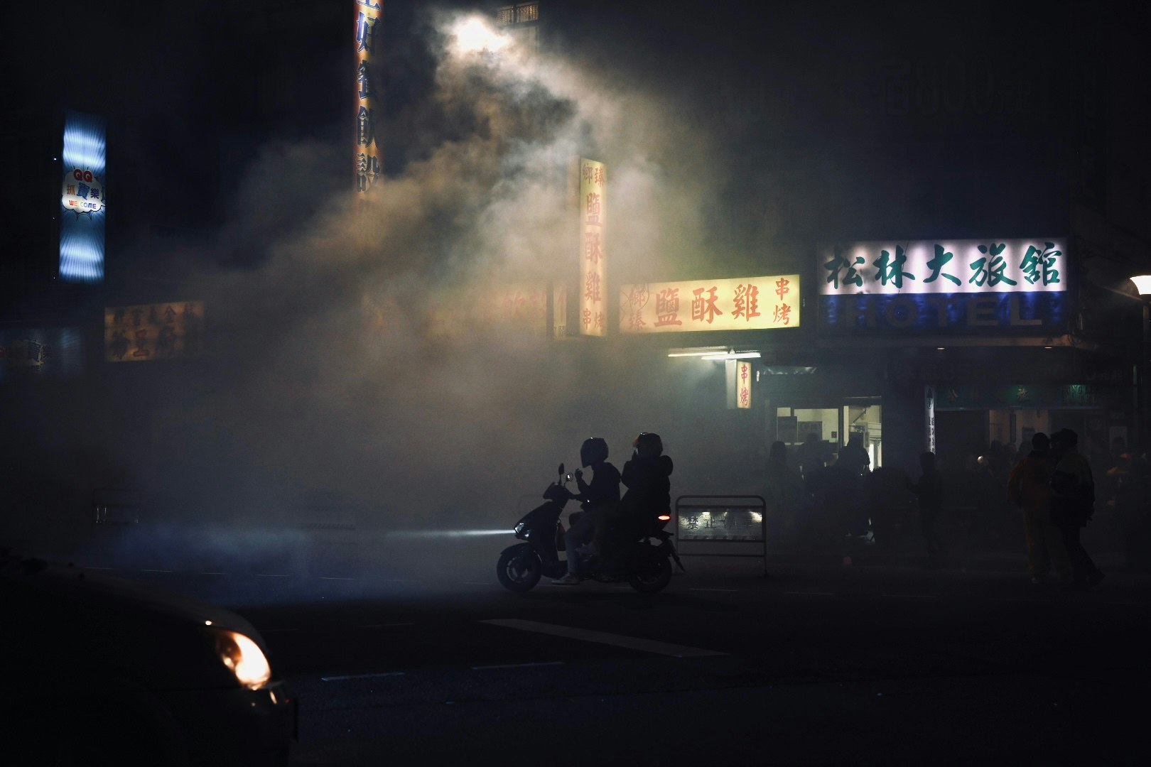 霧の夜にバイクと人影が並ぶ街角の看板前