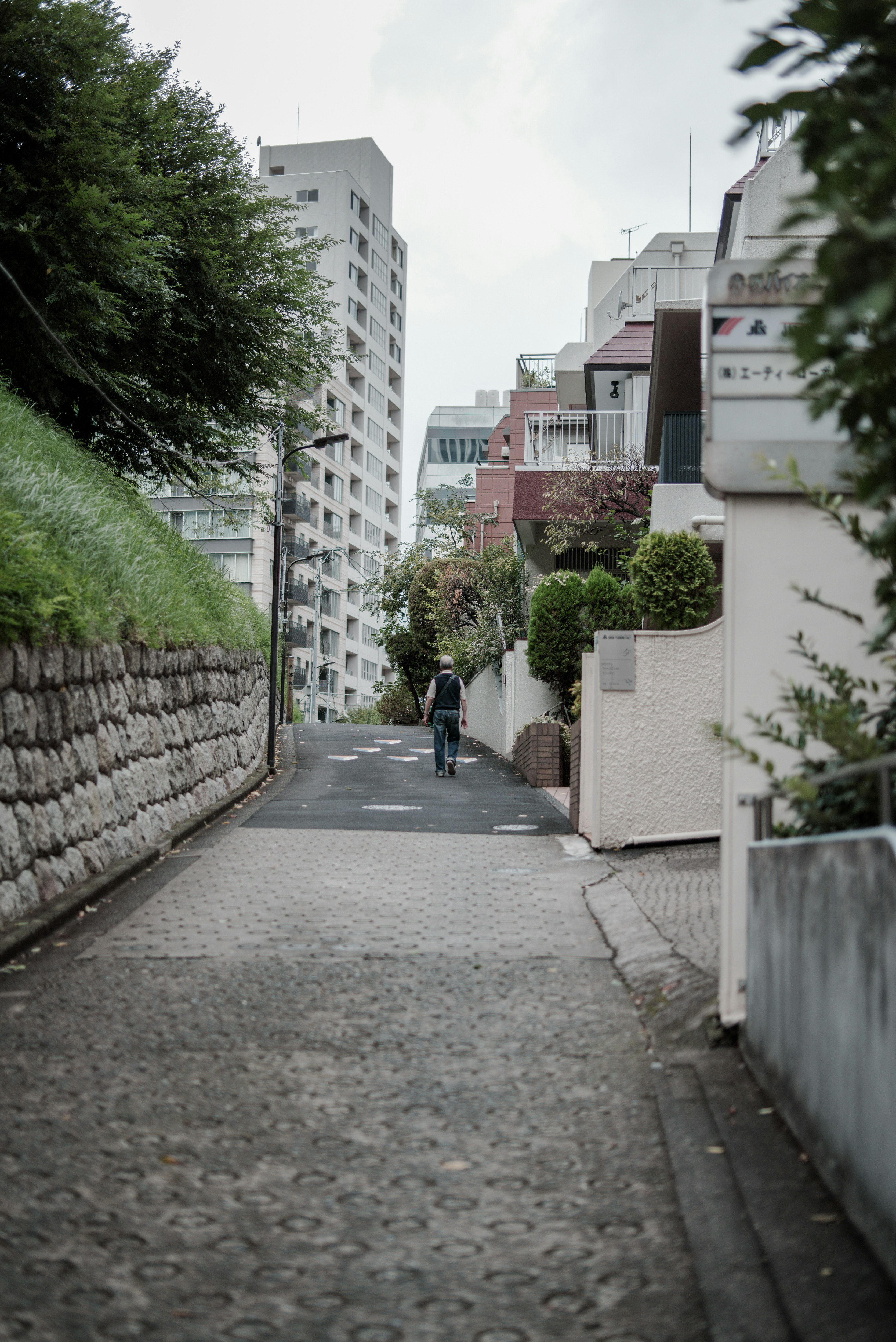 坂道の狭い路地を歩く人と集合住宅の並び