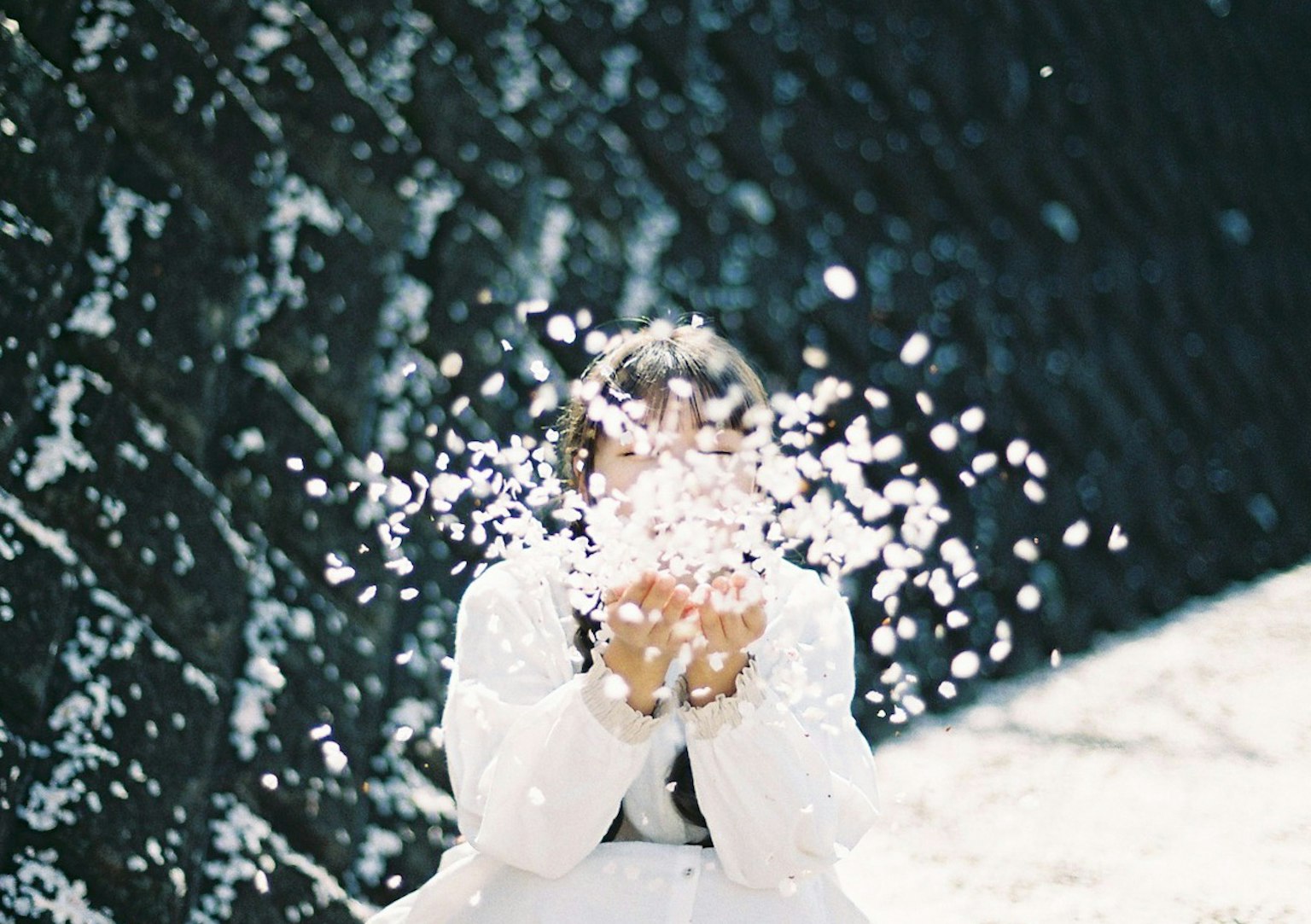 A woman in white clothing holding snow with a joyful expression