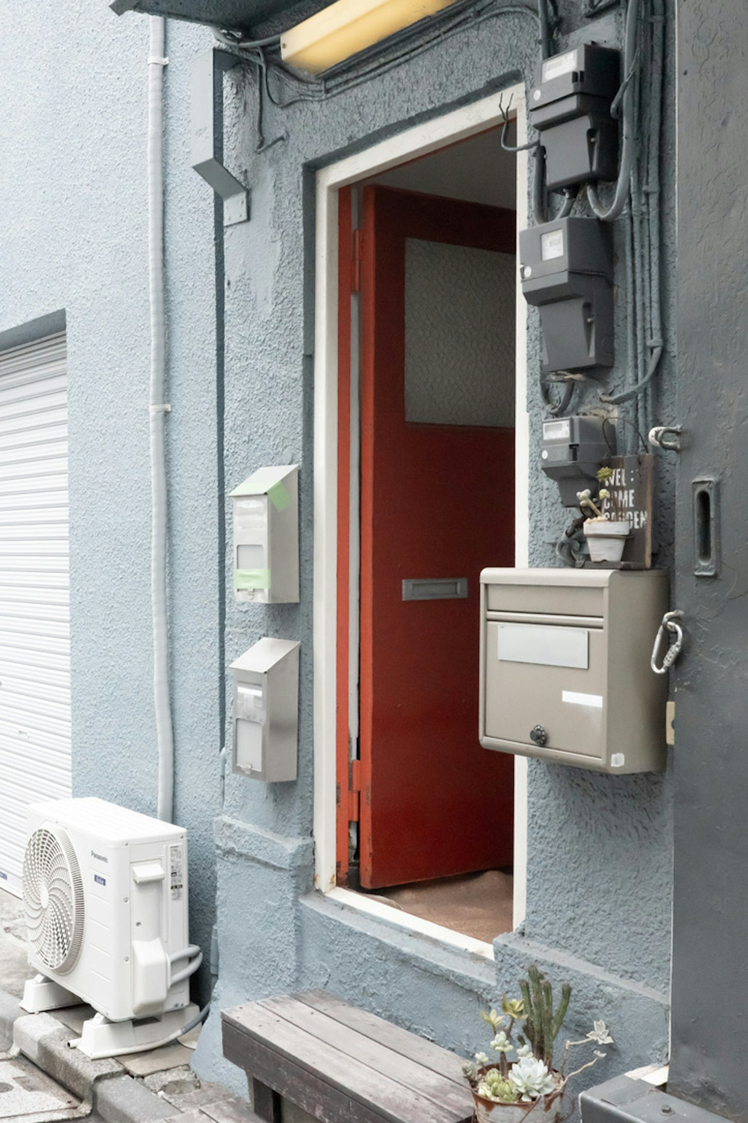 Entrée avec porte rouge sur mur gris avec boîte aux lettres et utilitaires
