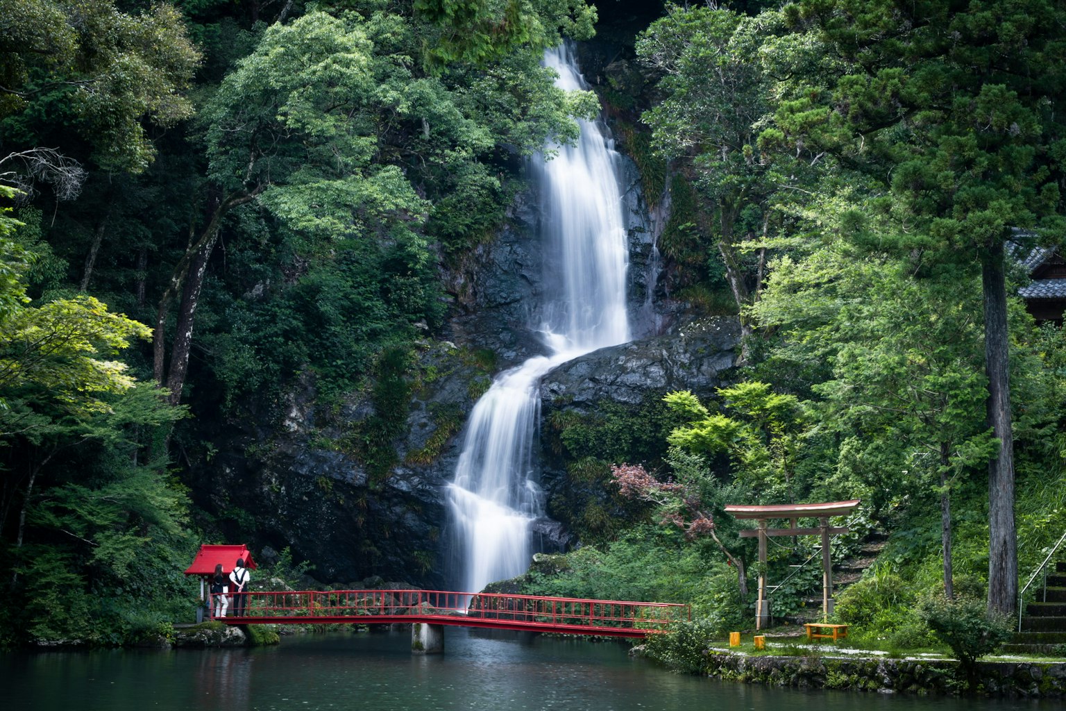 A scenic view featuring a waterfall surrounded by greenery and a red bridge